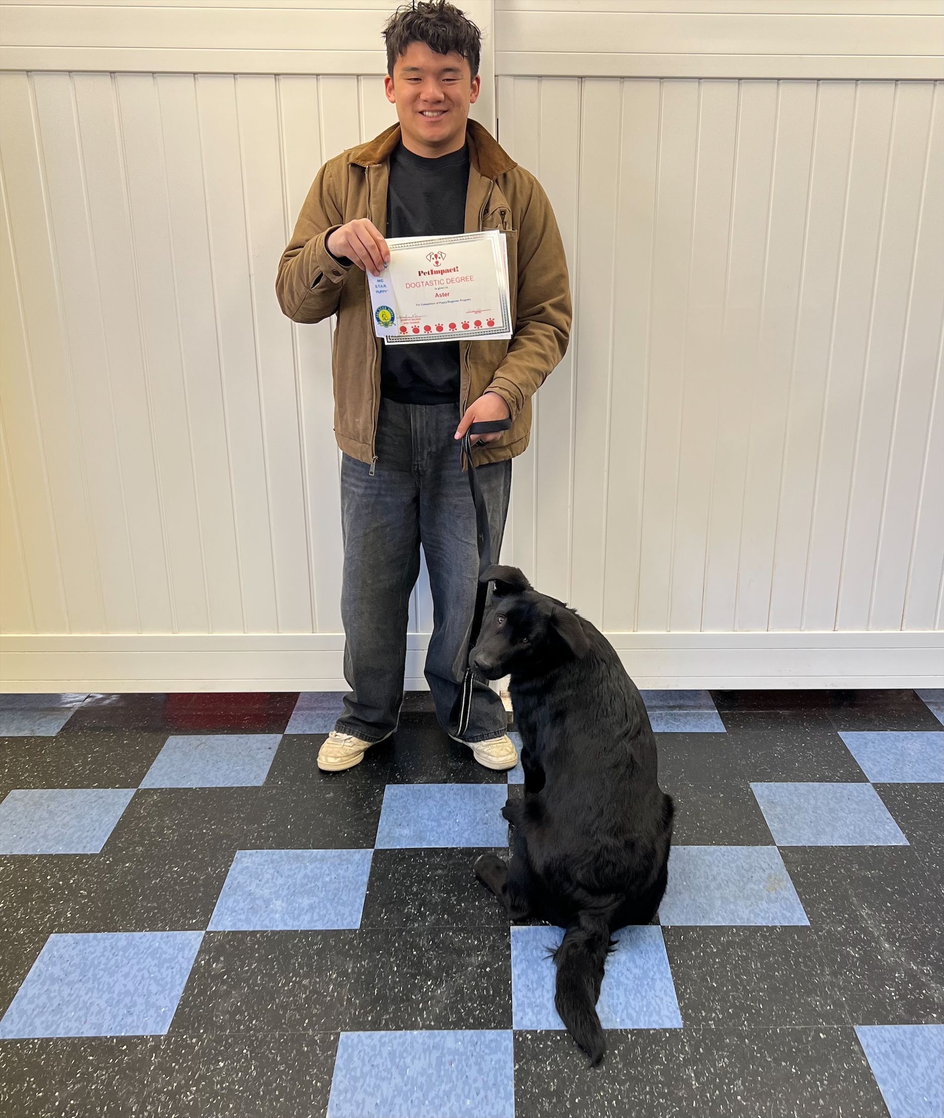 A boy is standing next to a black dog on a checkered floor.