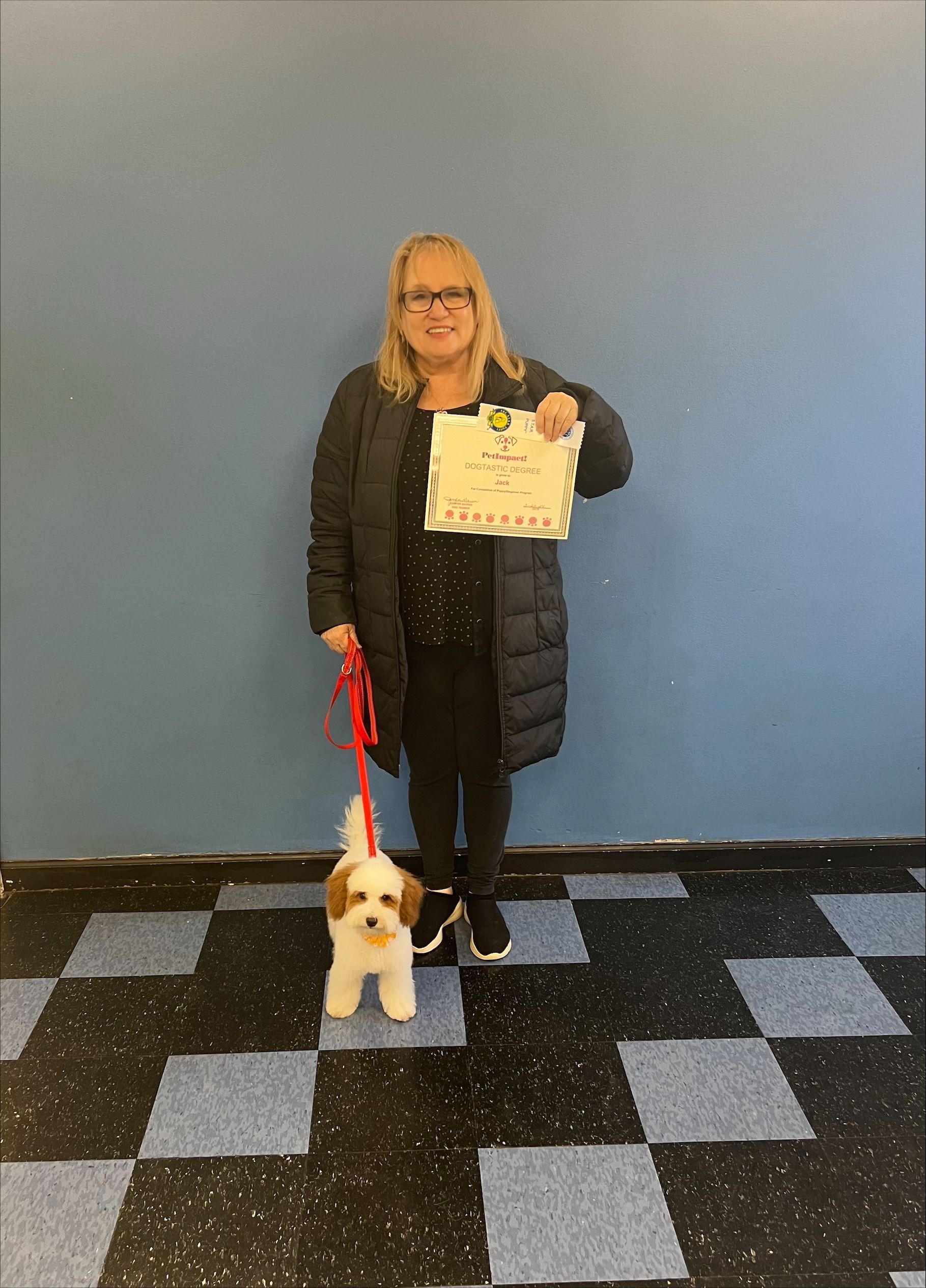 A woman is standing next to a small dog on a leash and holding a certificate.
