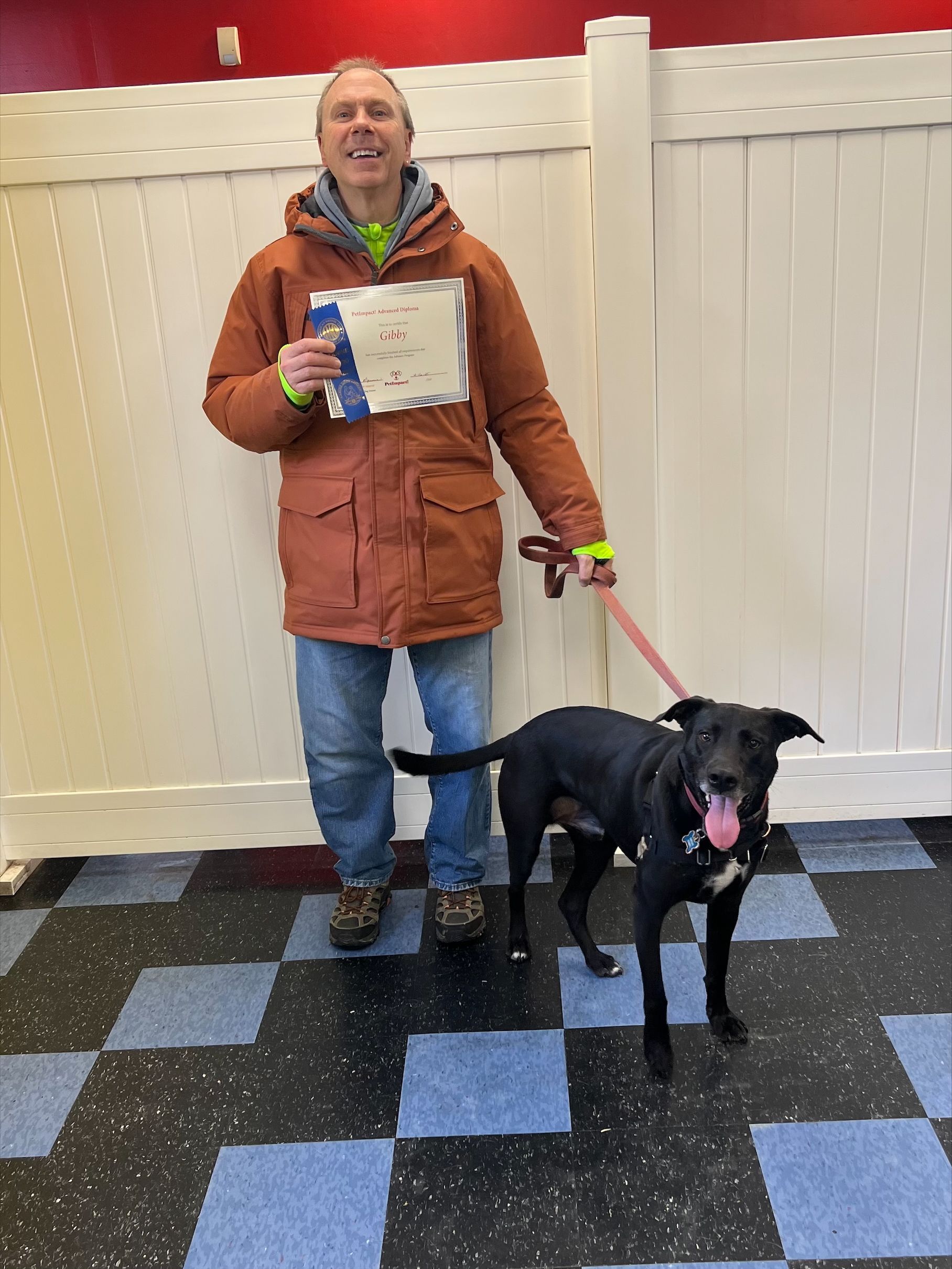 A man standing next to a black dog holding a certificate.