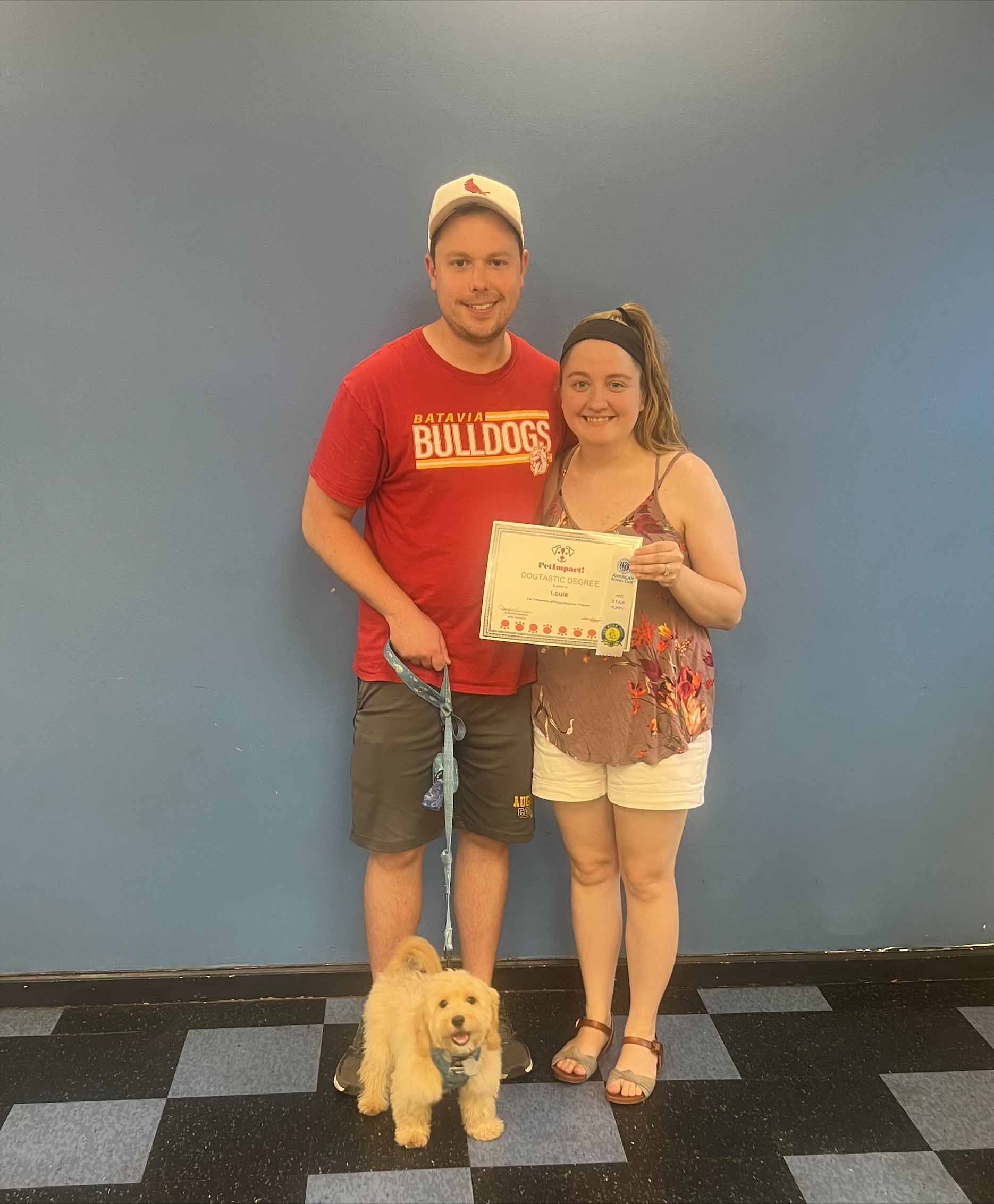 A Man And Woman Standing Next To A Small Dog Holding A Certificate