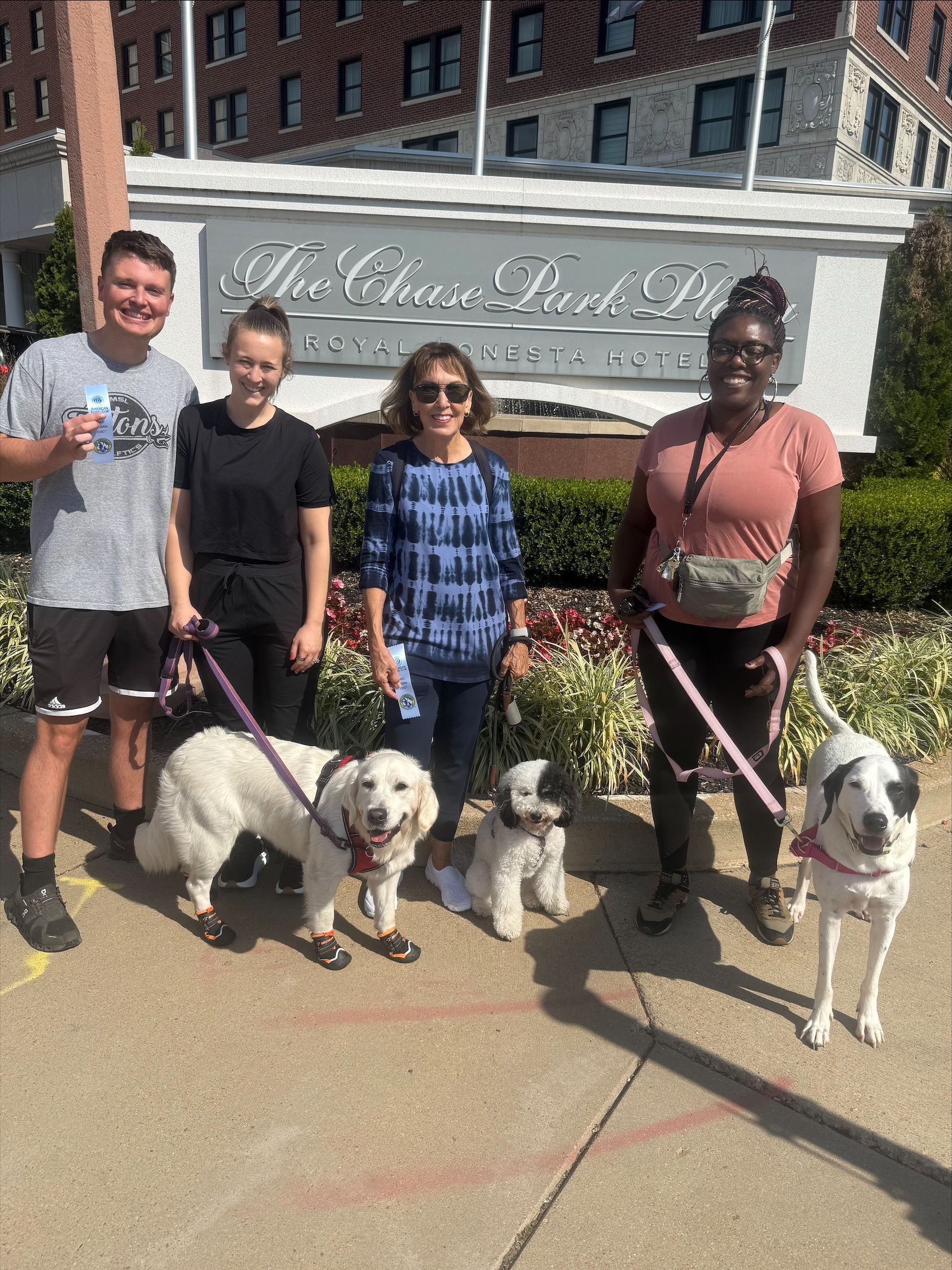 Four people stand with three dogs in front of a hotel.