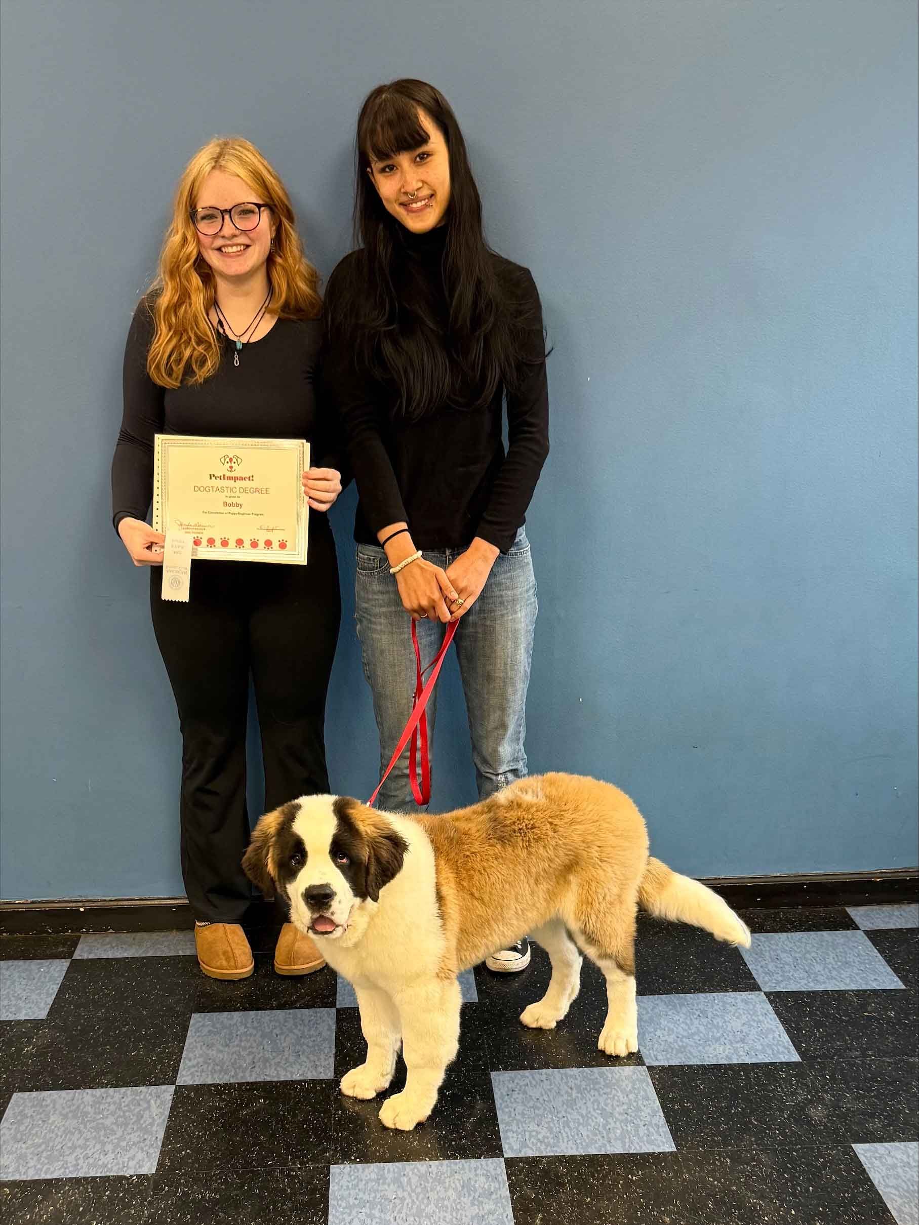 Two women are standing next to a brown and white dog on a leash.