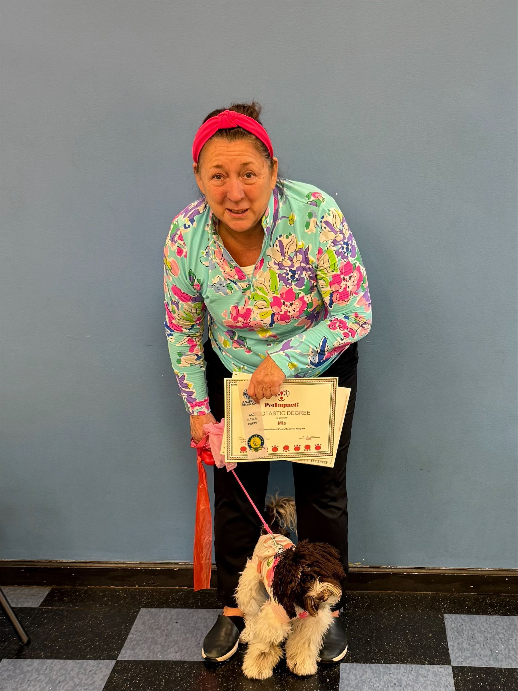 A woman is holding a cake and a dog on a leash.