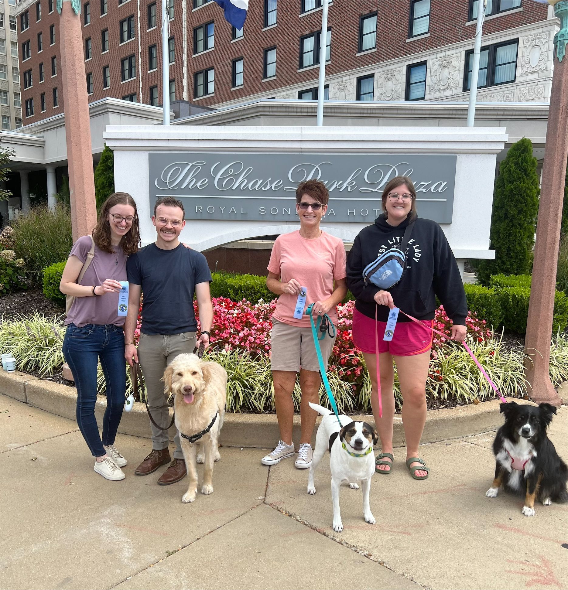 Four people with three dogs in front of The Chase Park Plaza hotel.