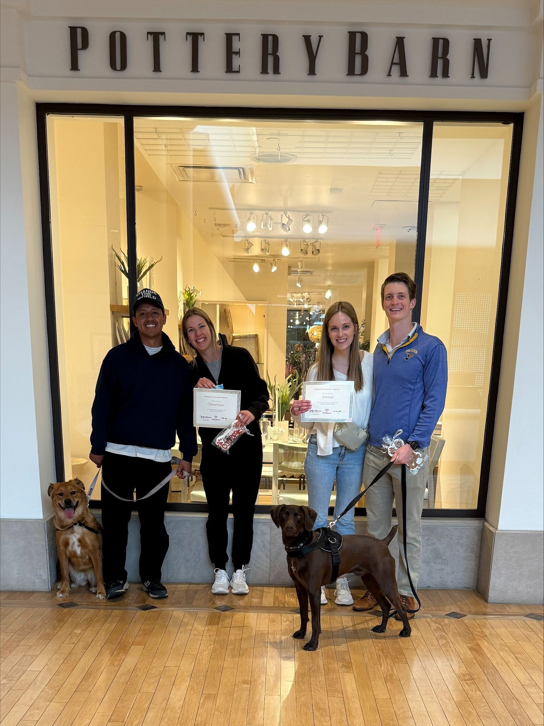 A group of people standing in front of a store with their dogs.