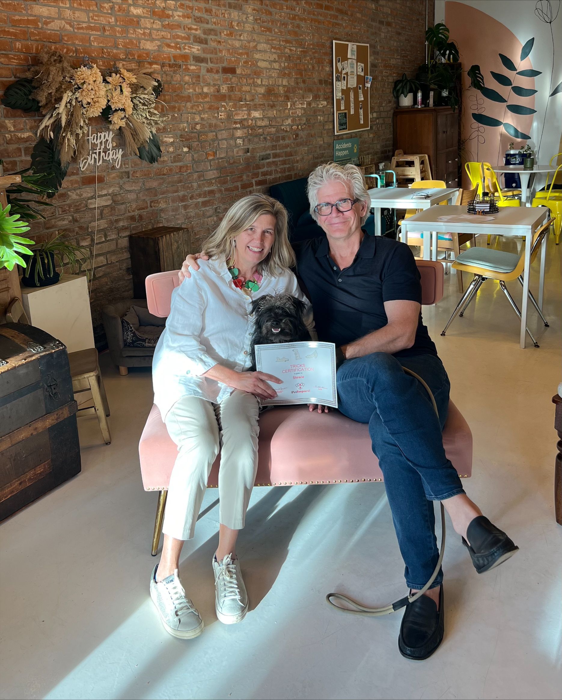 Two women are sitting on a couch with a dog and a laptop.