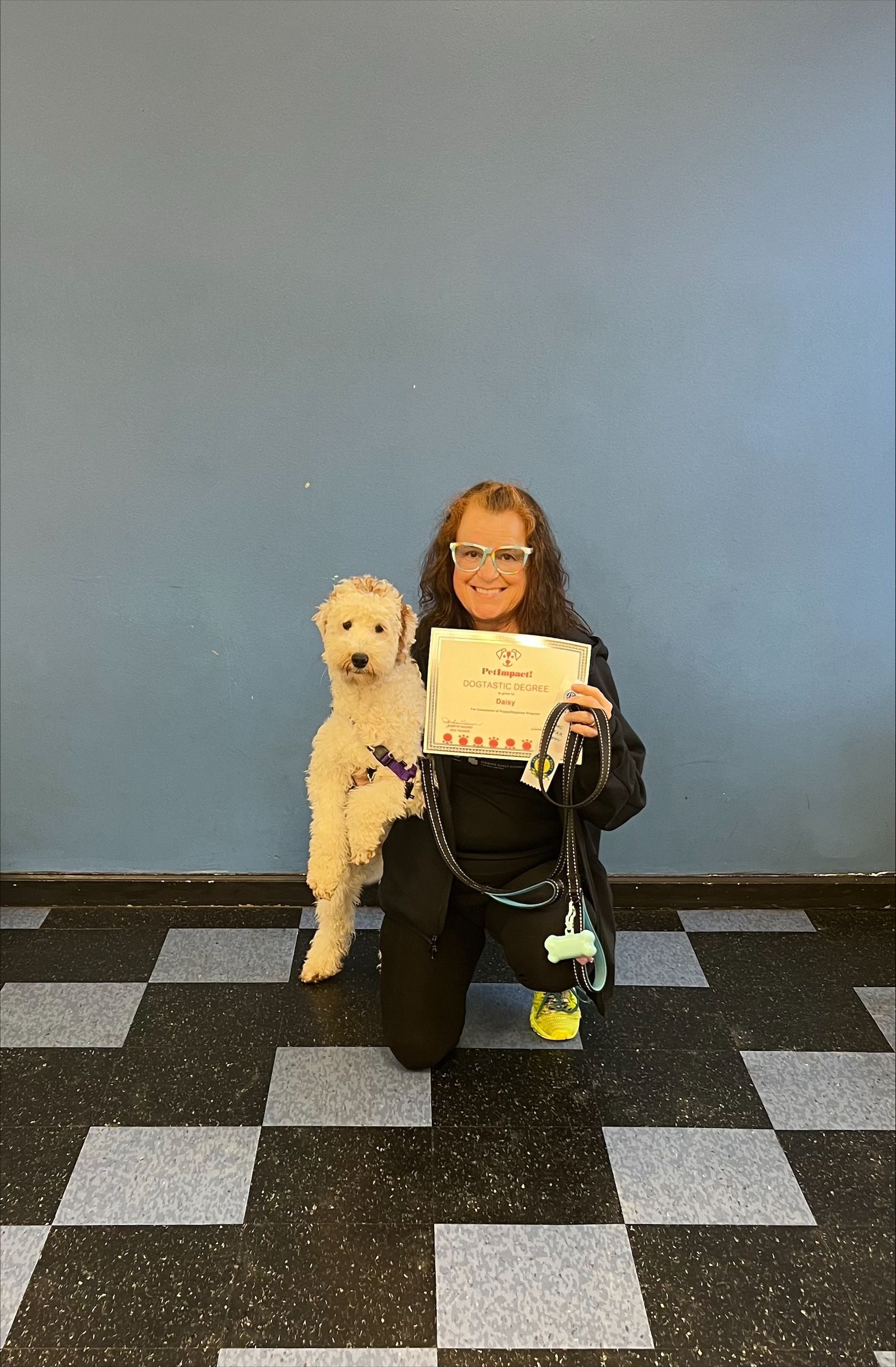 A woman is kneeling down next to a dog and holding a certificate.