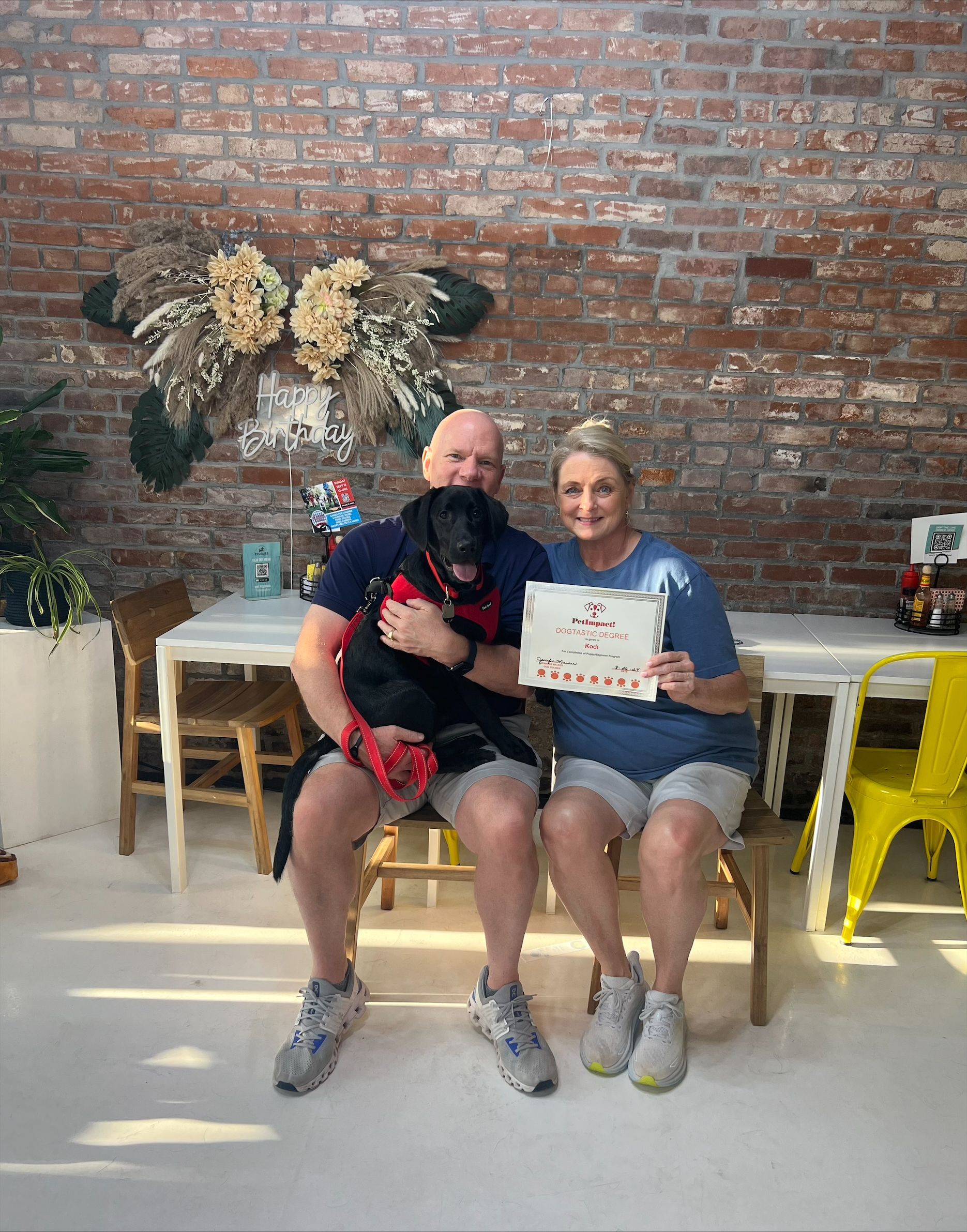 A man and a woman are sitting on a chair with a dog and holding a sign.