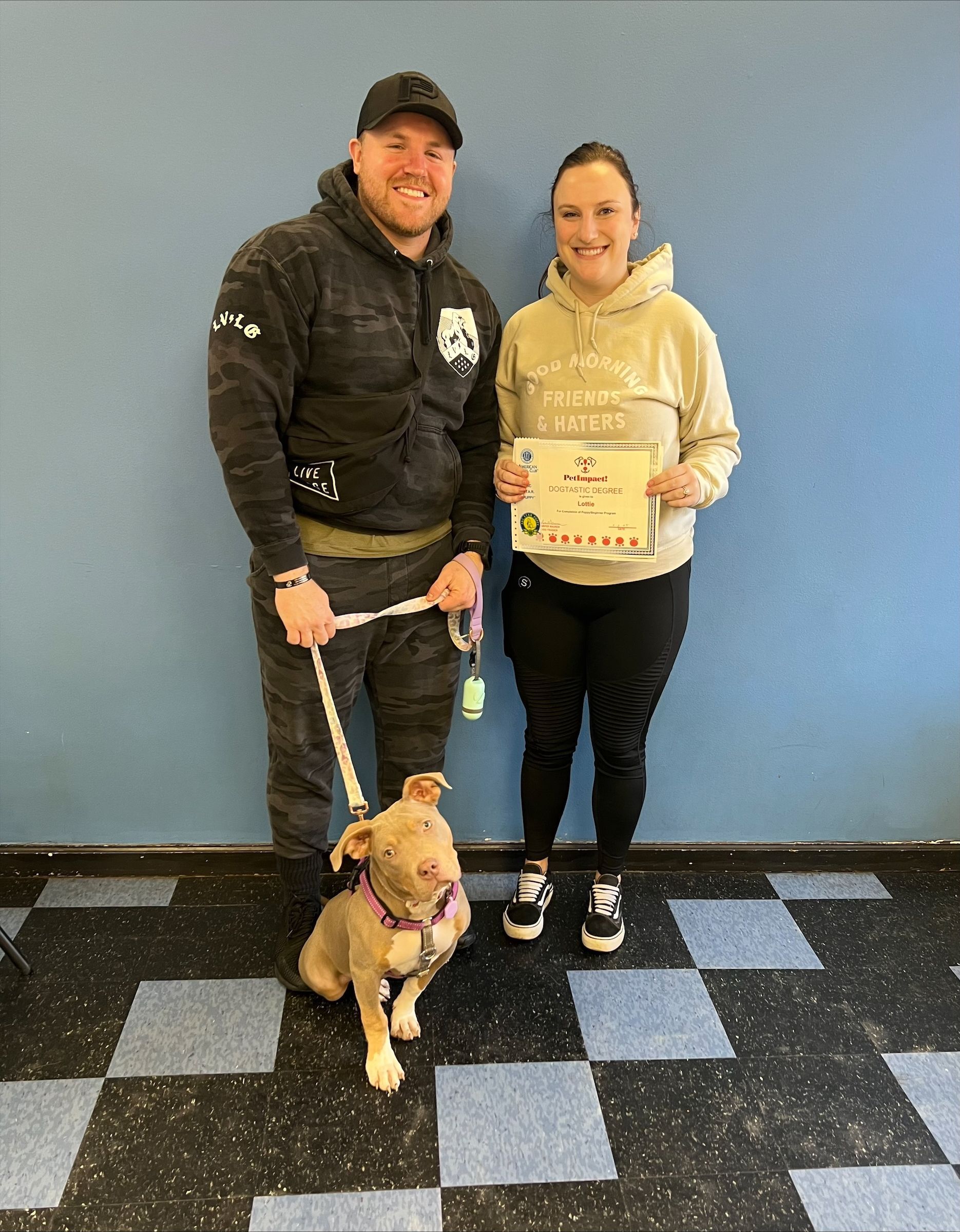 A man and a woman are standing next to a dog on a leash.