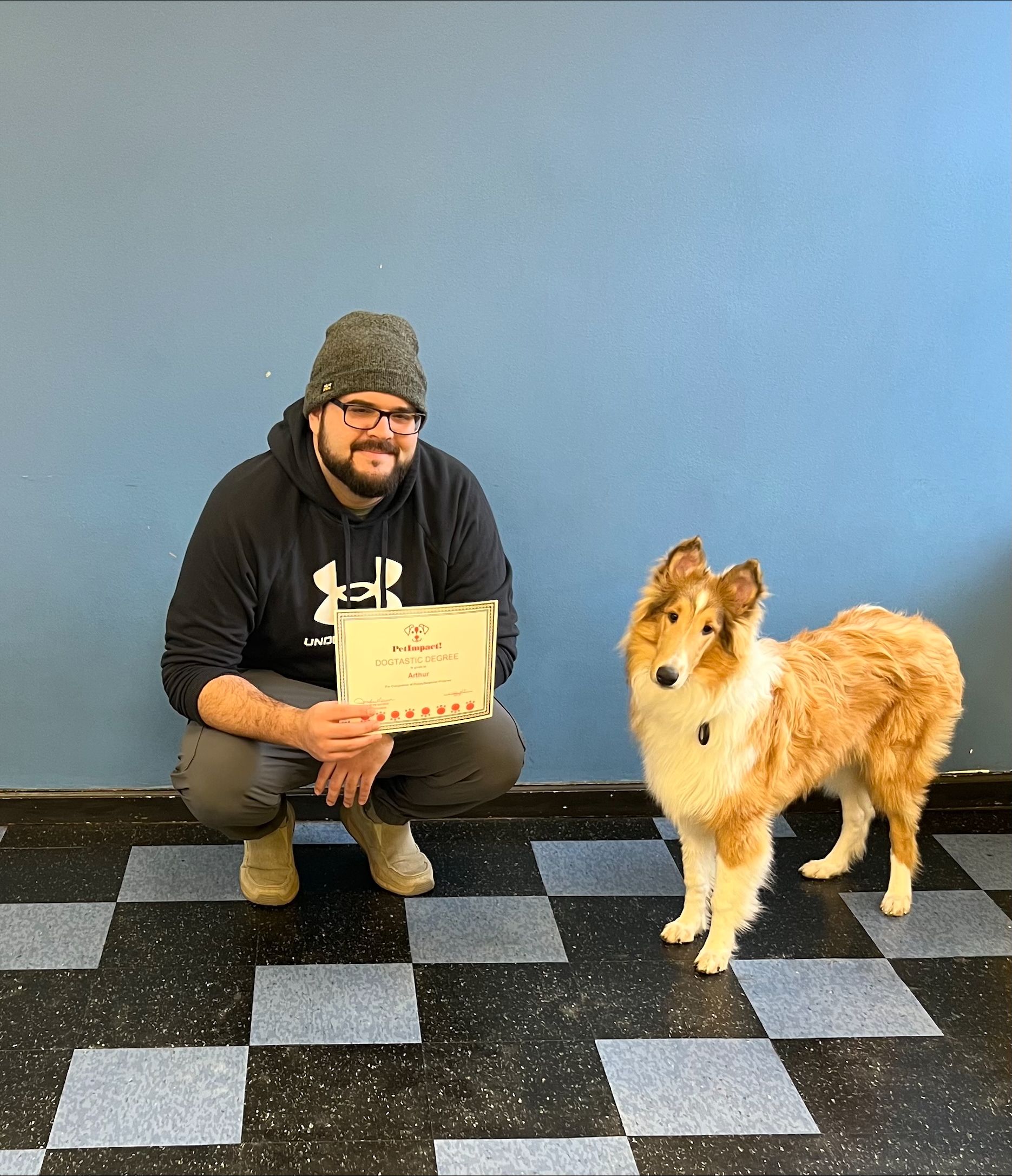A man is kneeling down next to a dog holding a certificate.