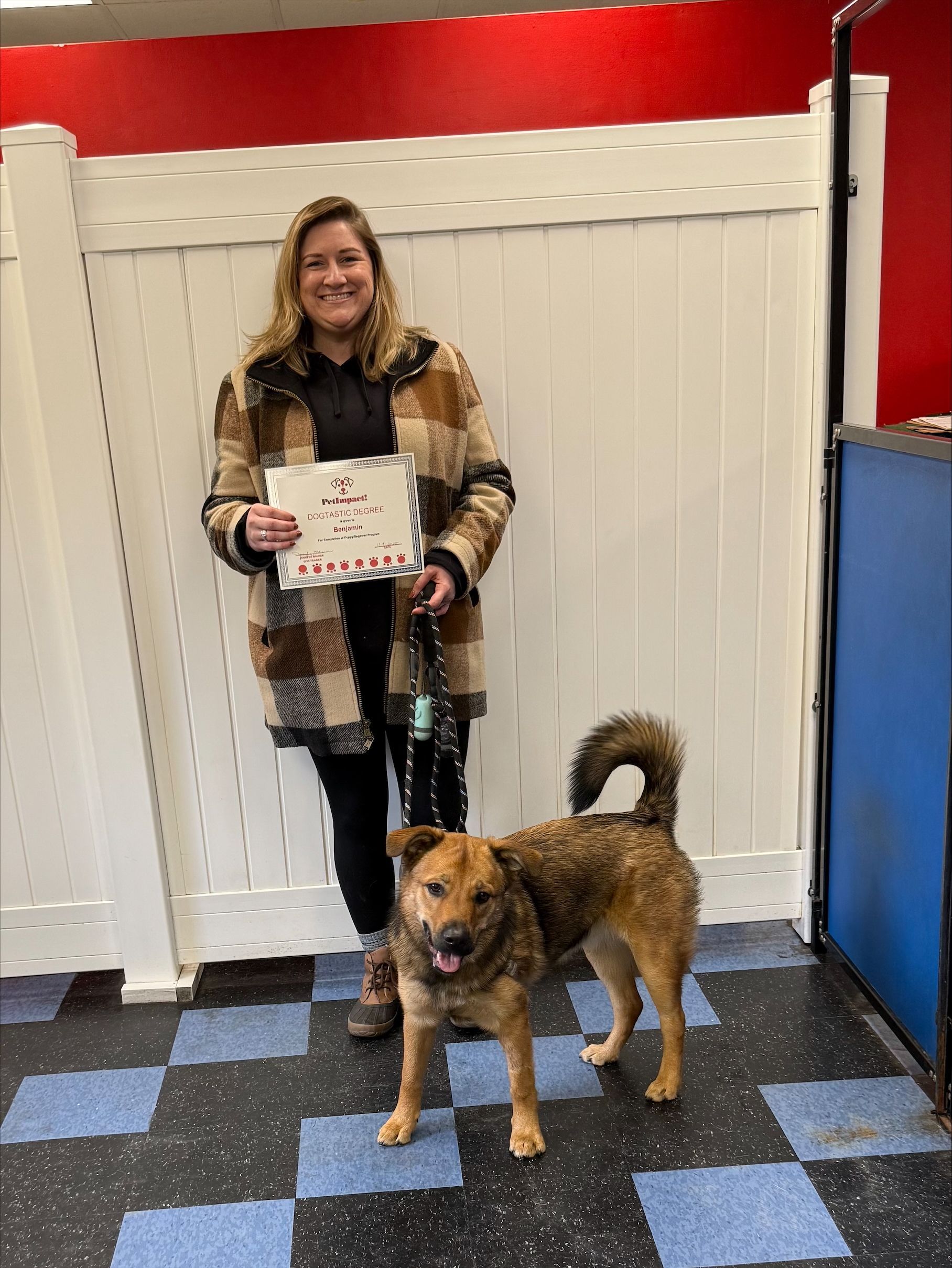 Woman and dog posing indoors. Woman holding certificate, dog stands at her side.