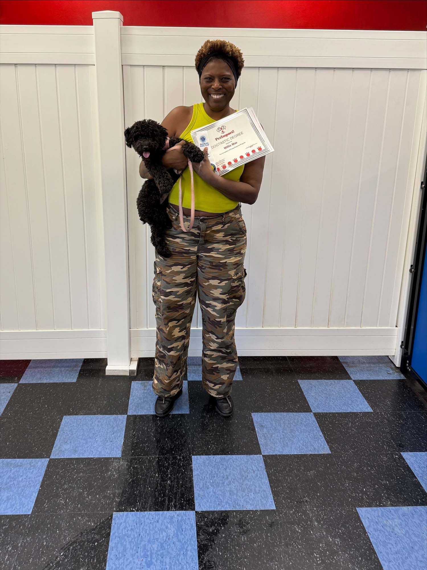 A woman is holding a small black dog and a certificate.