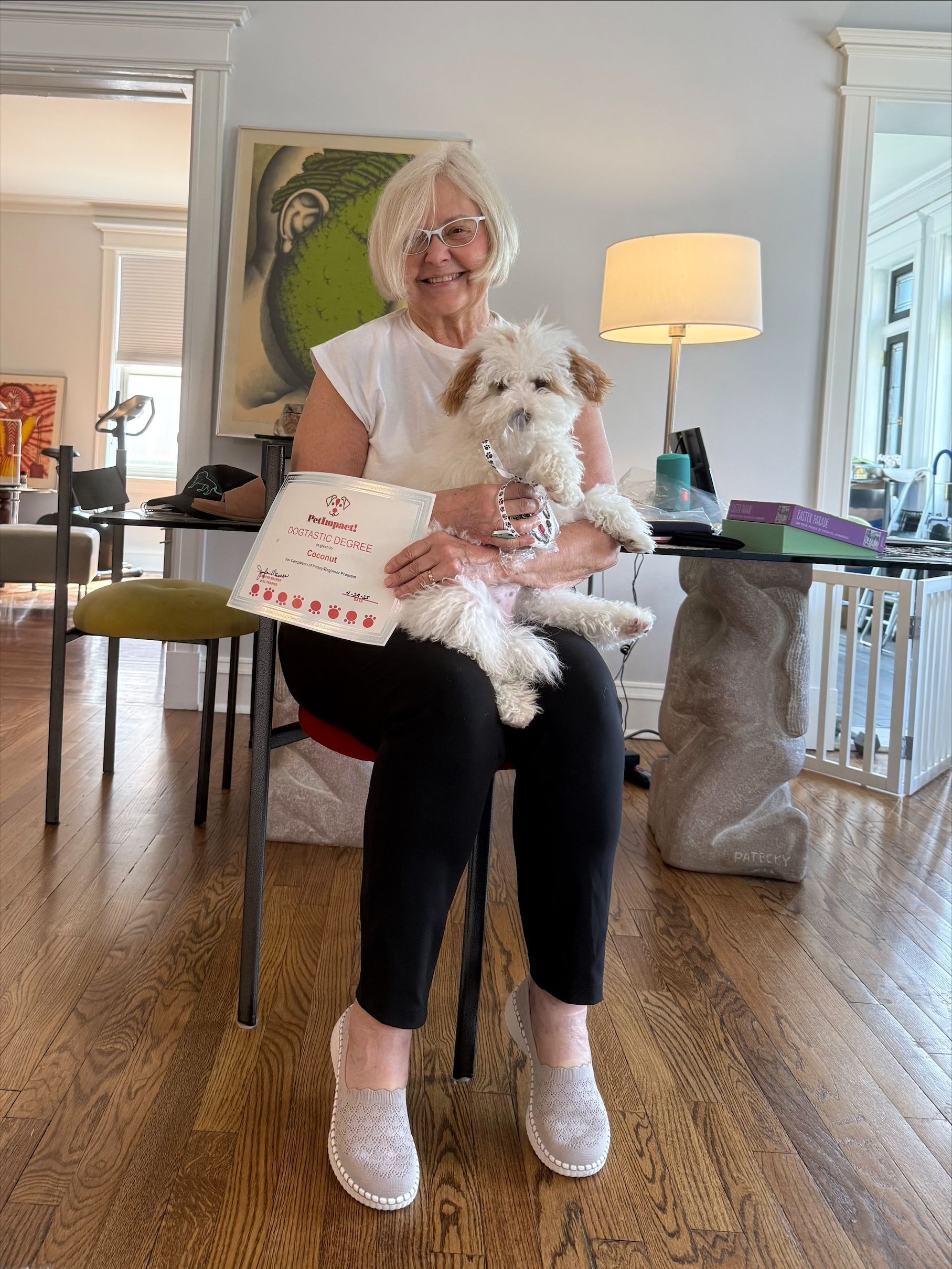 A woman is sitting on a chair holding a small white dog.