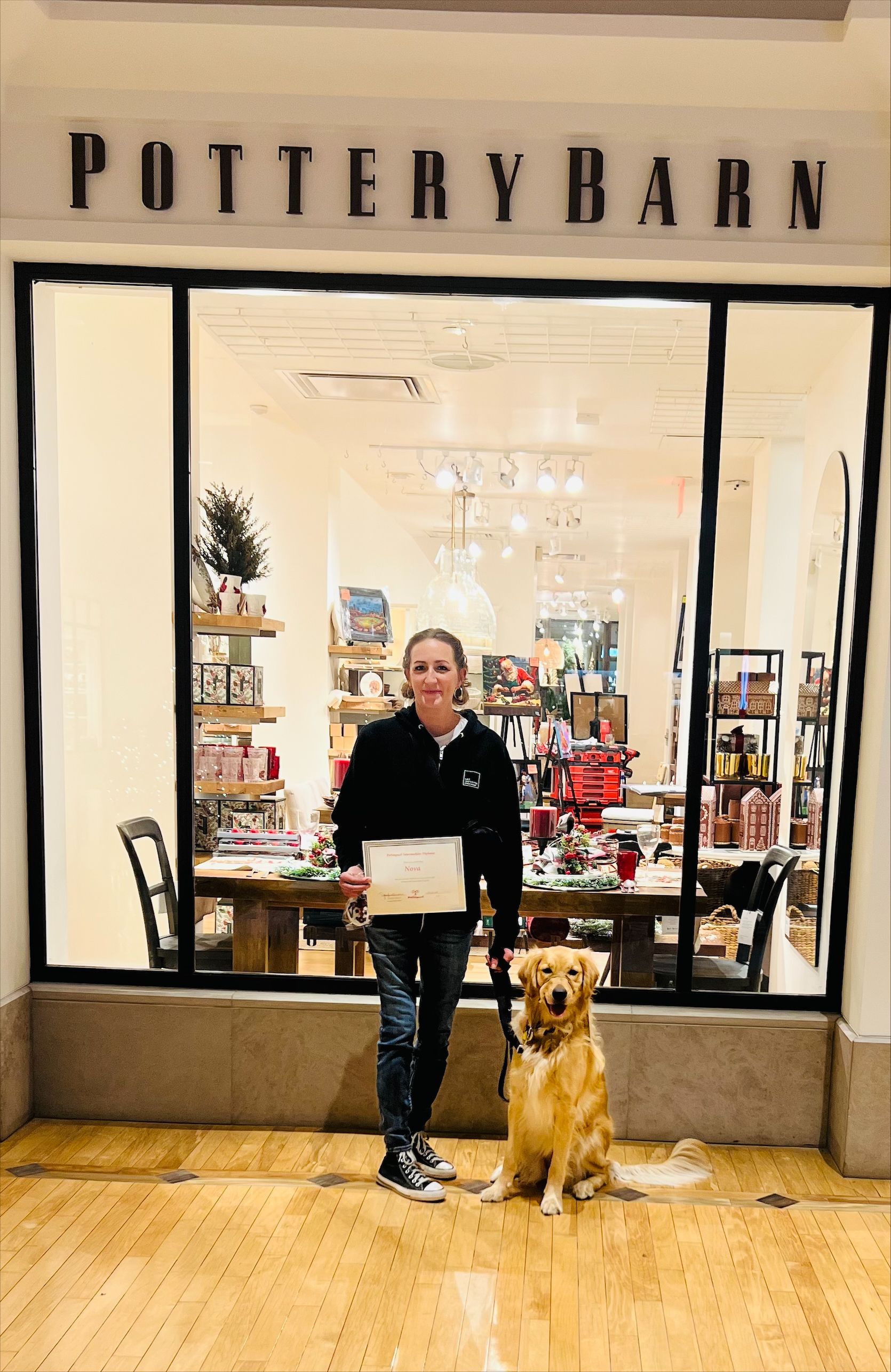 Woman and golden retriever in front of Pottery Barn store, holding certificate.