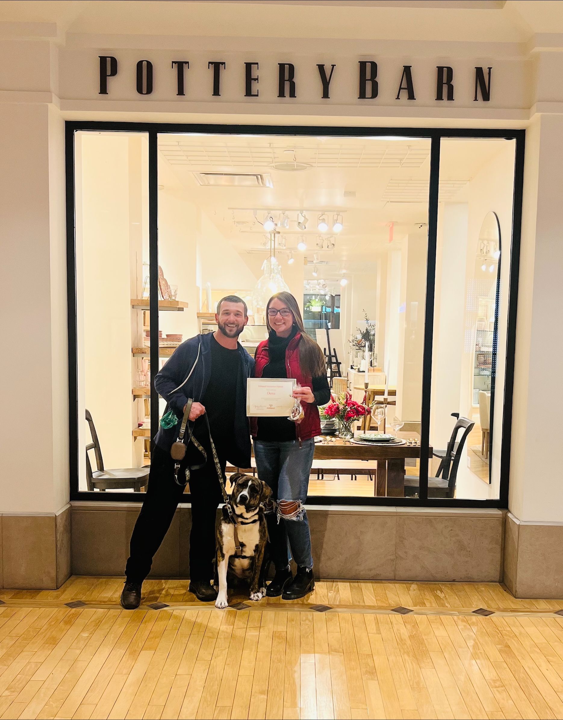 A man and a woman are standing in holding a certificate and a dog.