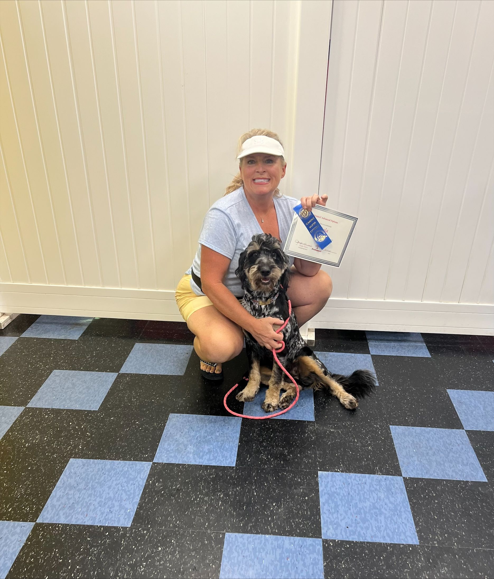 A woman is kneeling down next to a dog on a checkered floor.