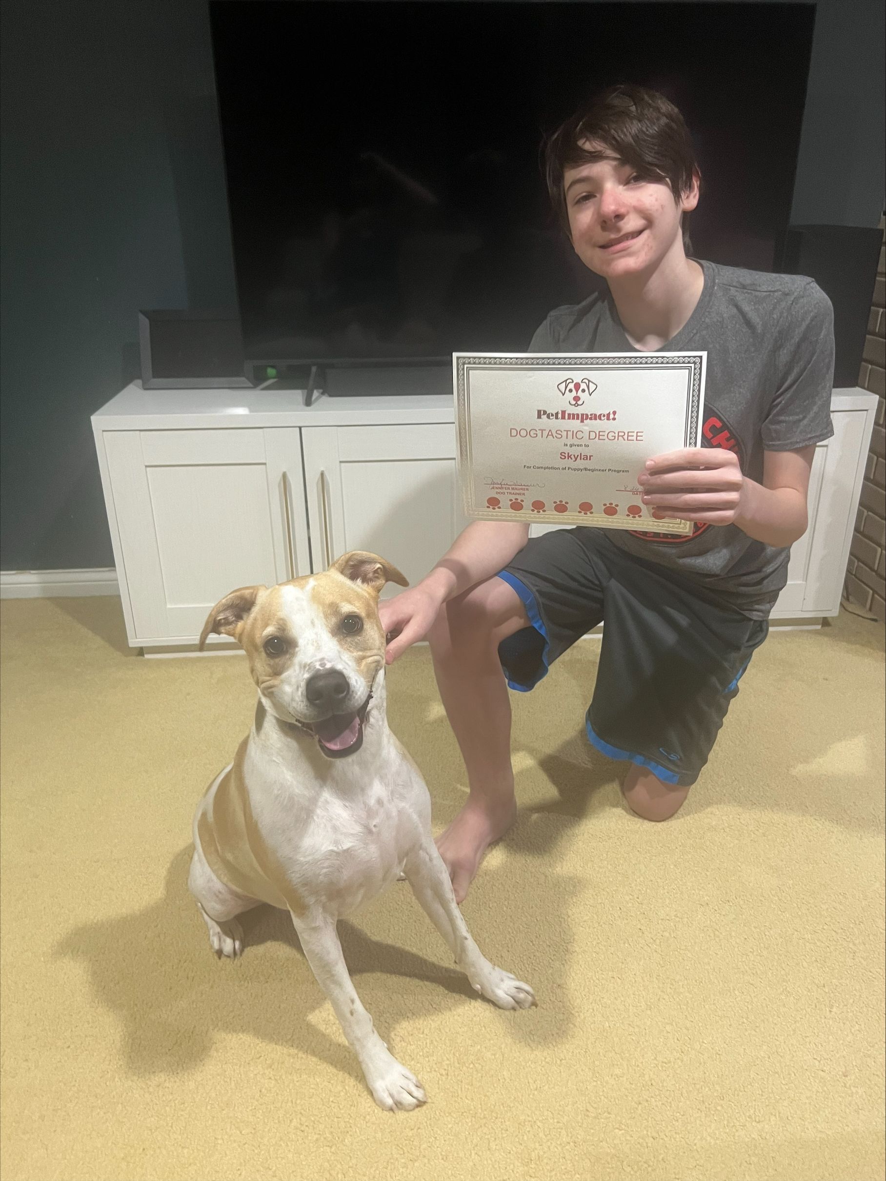 A boy is kneeling down next to a dog and holding a certificate.