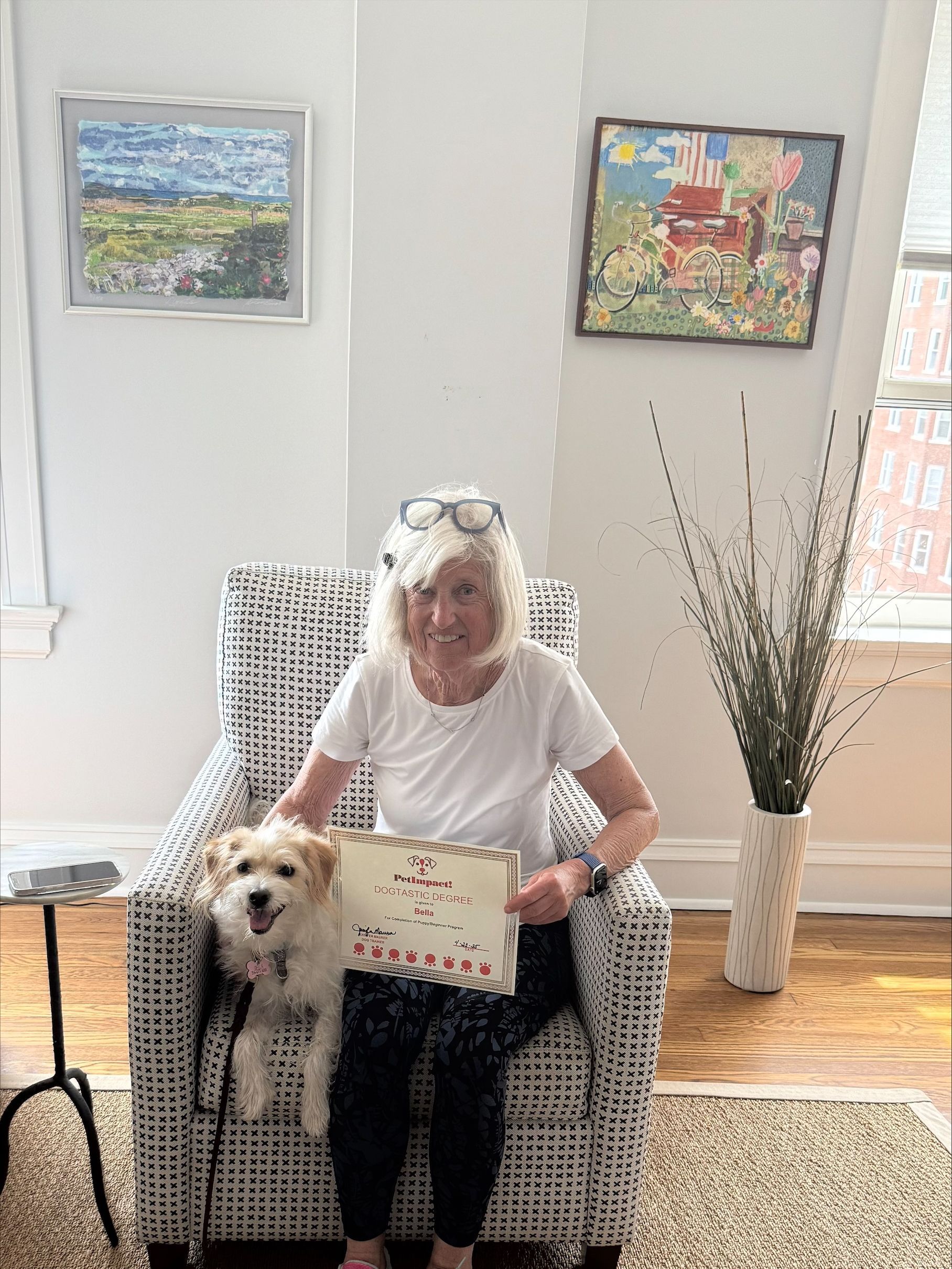 A woman is sitting in a chair with a dog and holding a book.