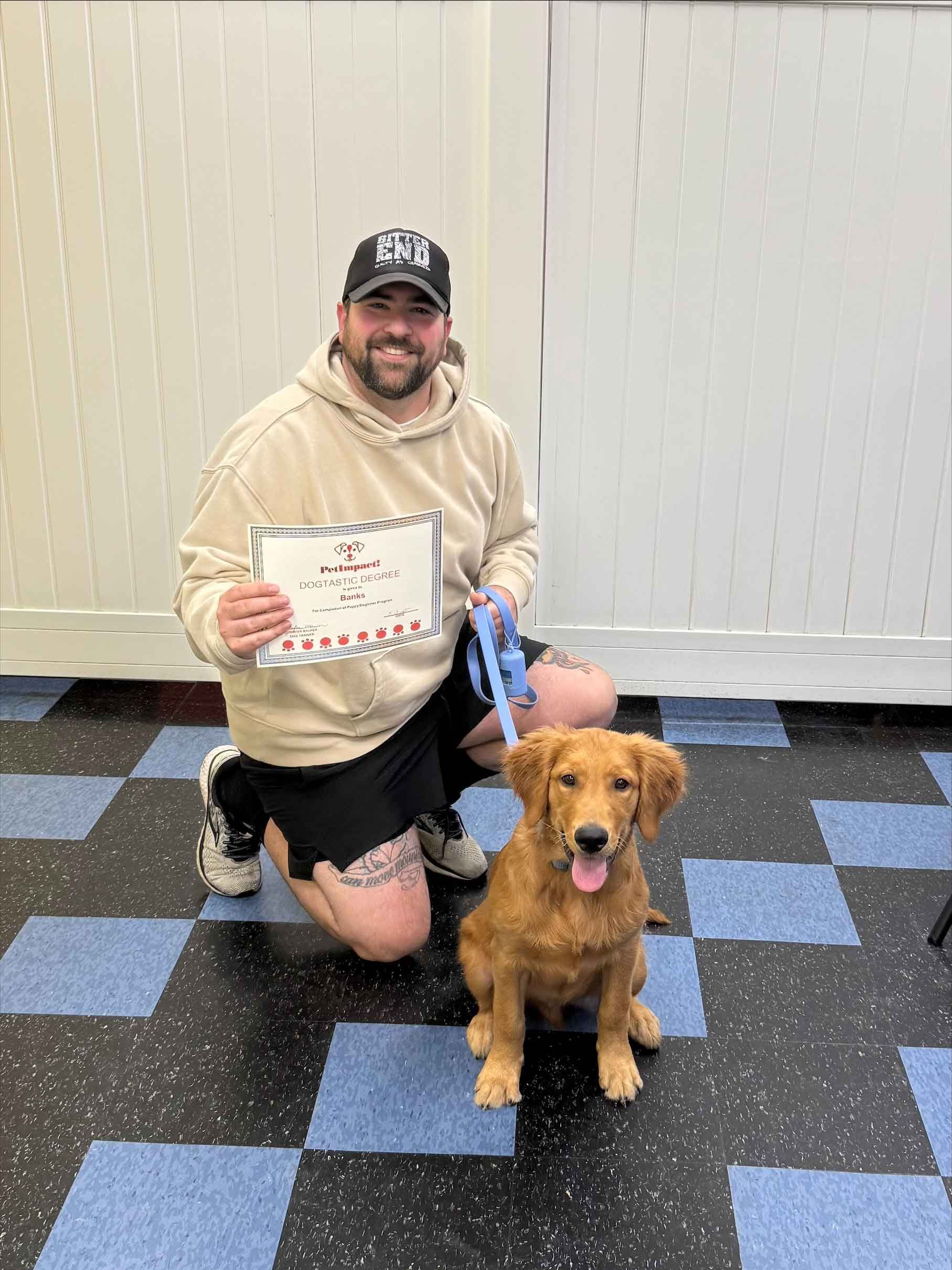 A man is kneeling down next to a puppy and holding a certificate.
