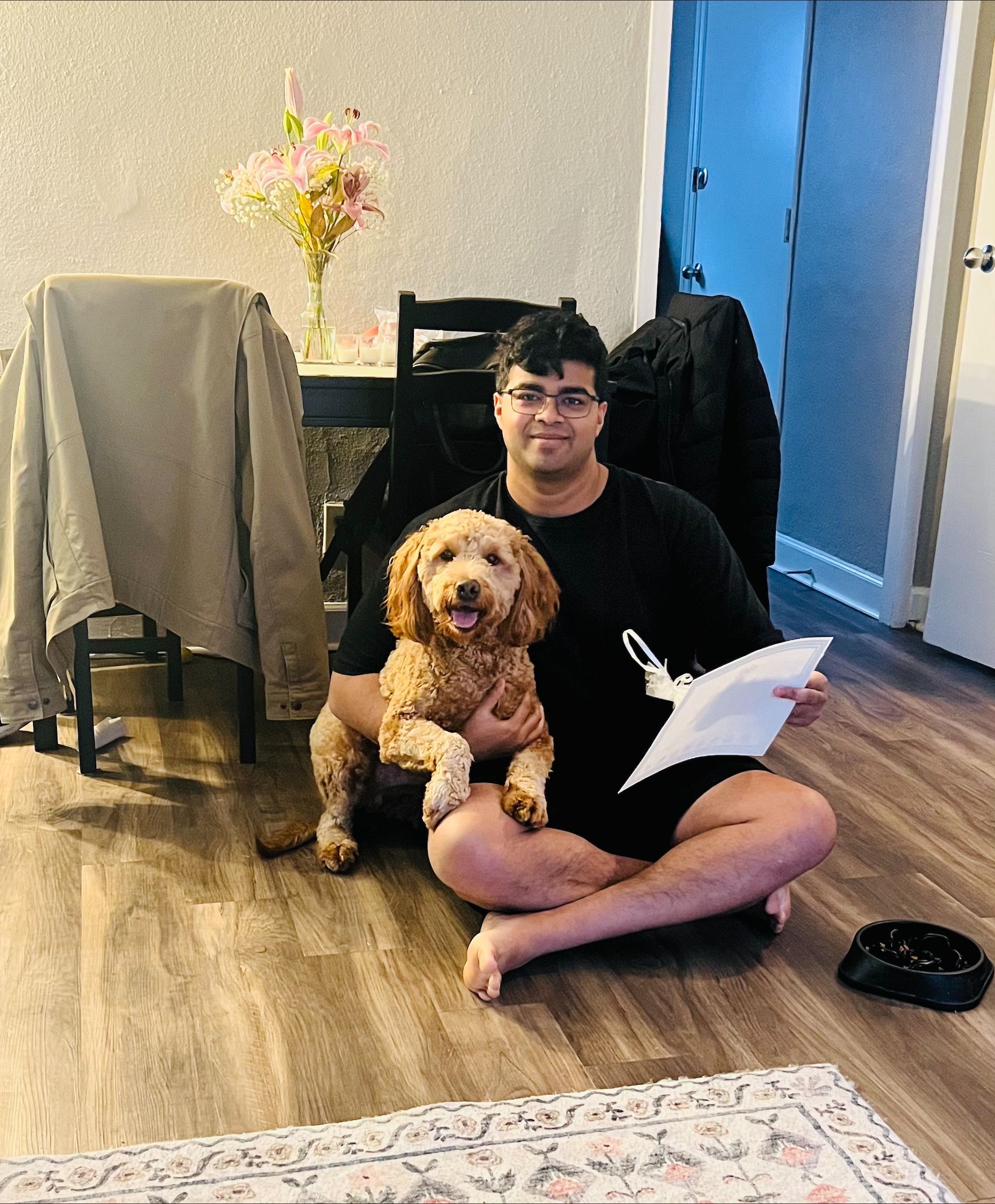 A man is sitting on the floor holding a dog and a piece of paper.
