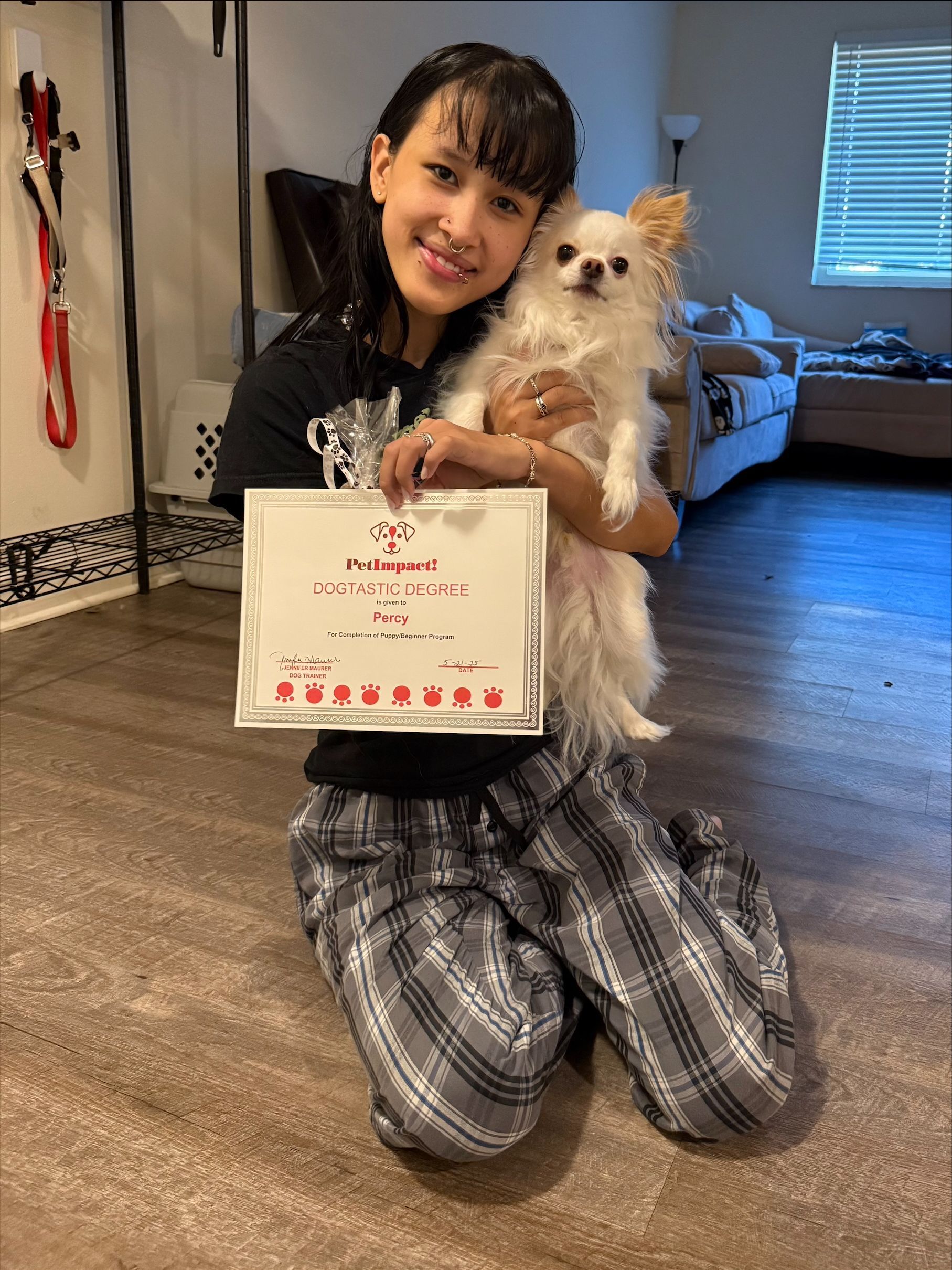 A girl is kneeling on the floor holding a small white dog and a certificate.