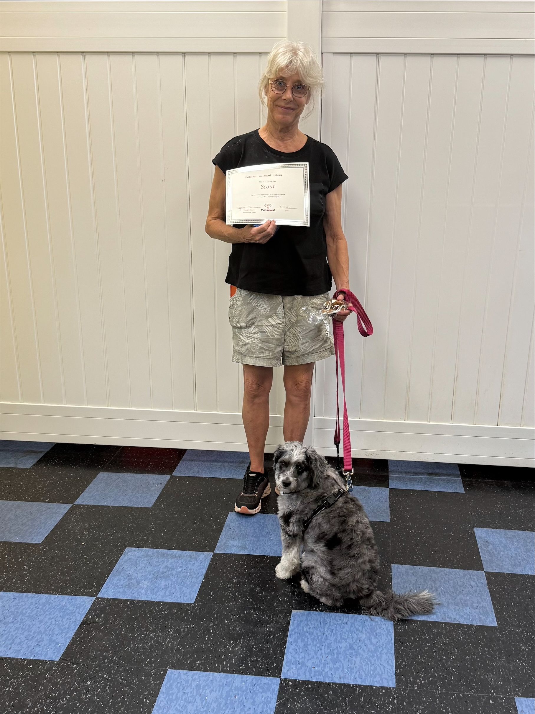 Woman and dog pose with certificate in front of white and blue wall; dog sitting and looking at camera.