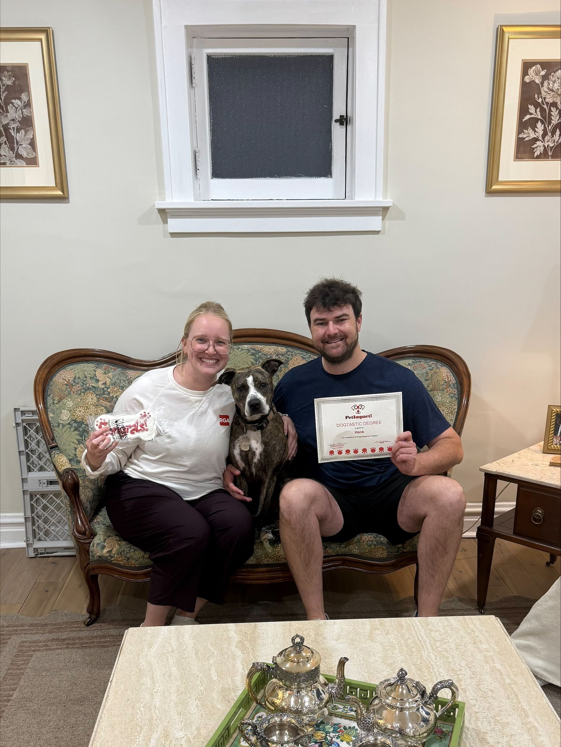 Two people are sitting on a couch, smiling and holding a certificate.