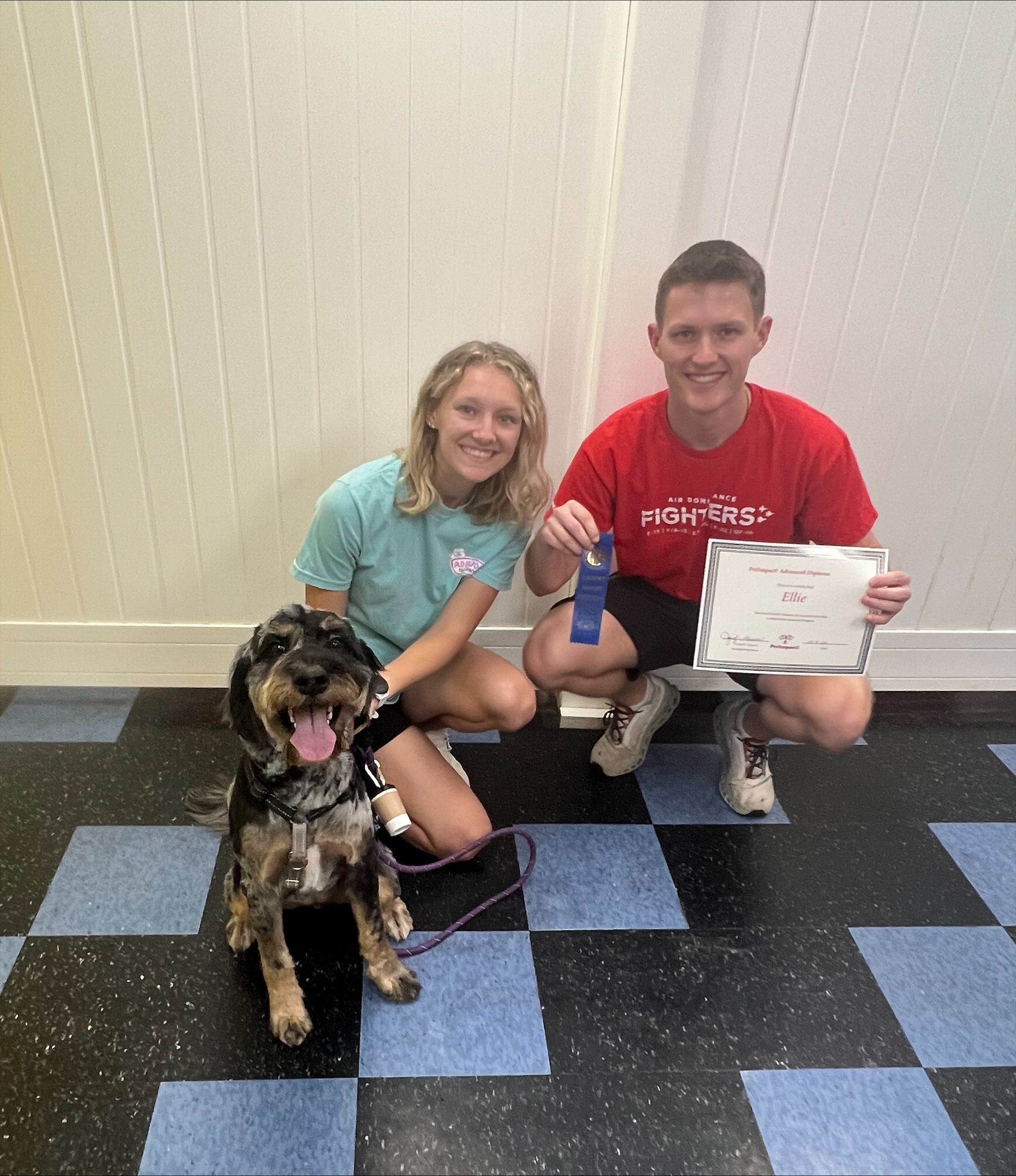 A man in a red shirt is kneeling next to a woman and a dog