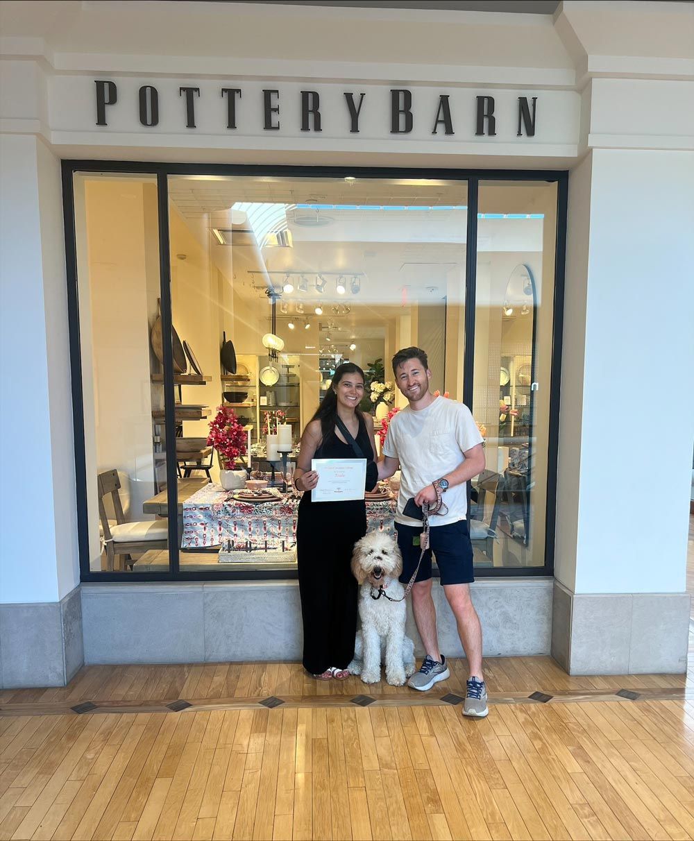 A man and woman standing with a dog in front of a pottery barn store