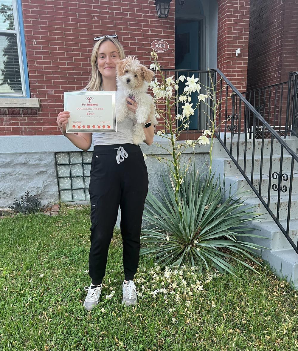 A woman is holding a dog and a certificate in front of a brick house.