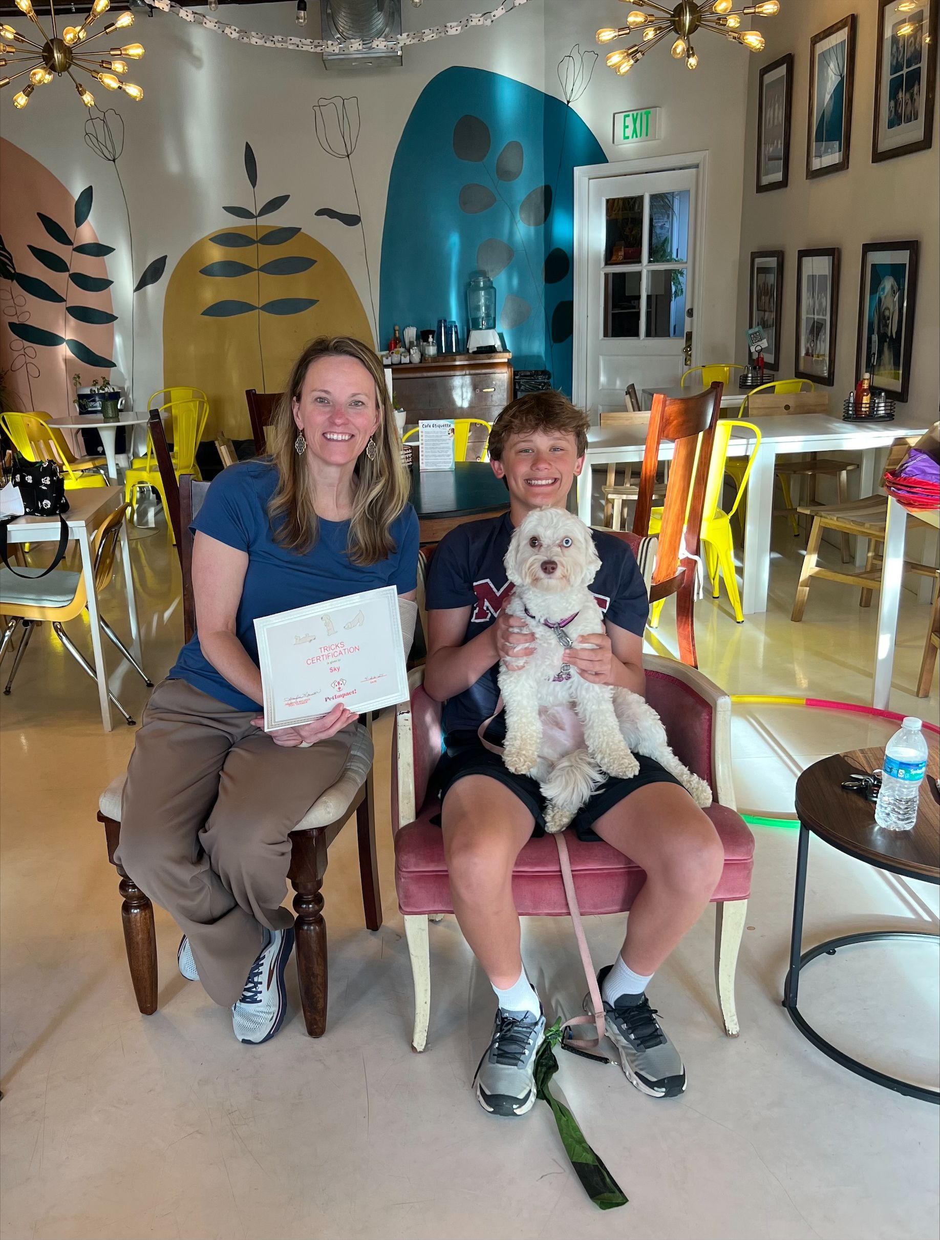 A man and a woman are sitting in chairs holding a white dog.