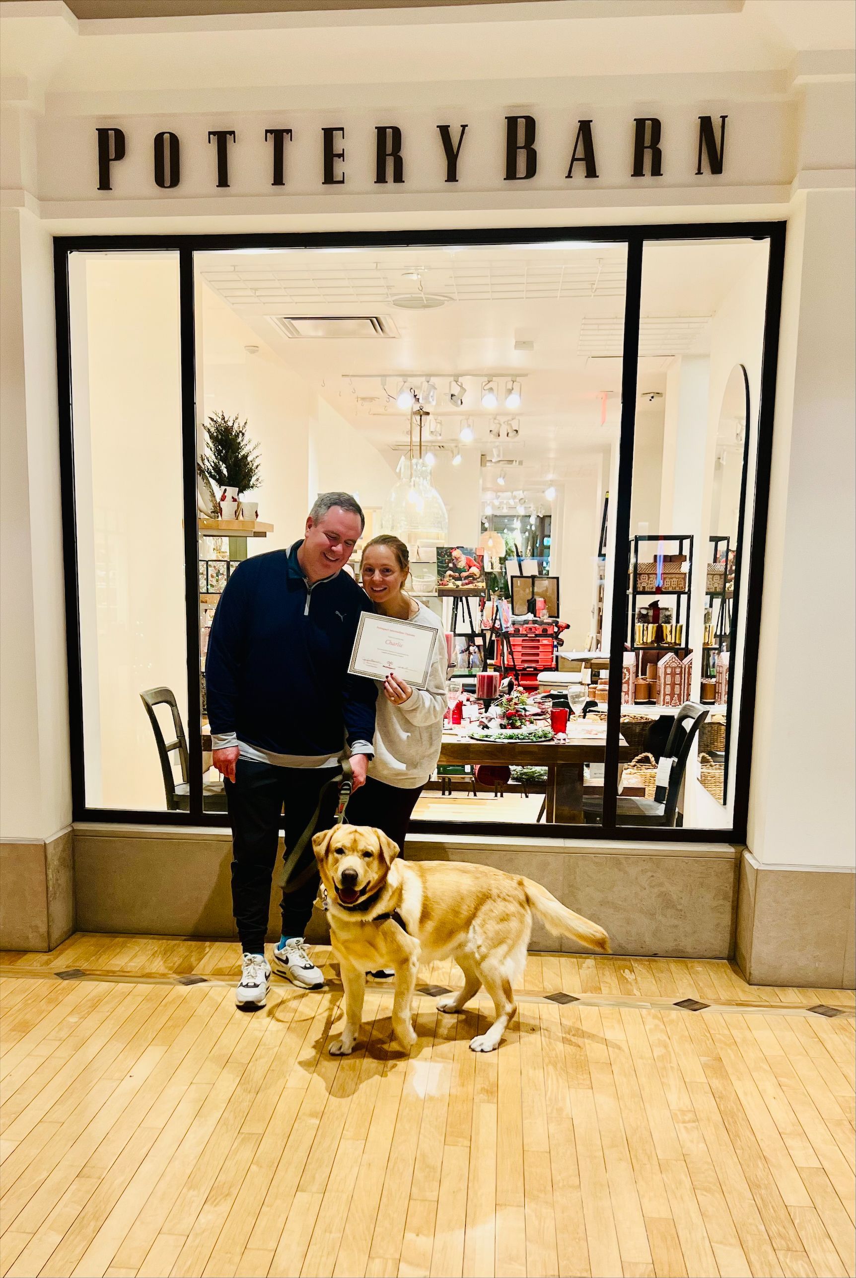 Couple and dog pose in front of a Pottery Barn storefront. The dog is a yellow labrador.