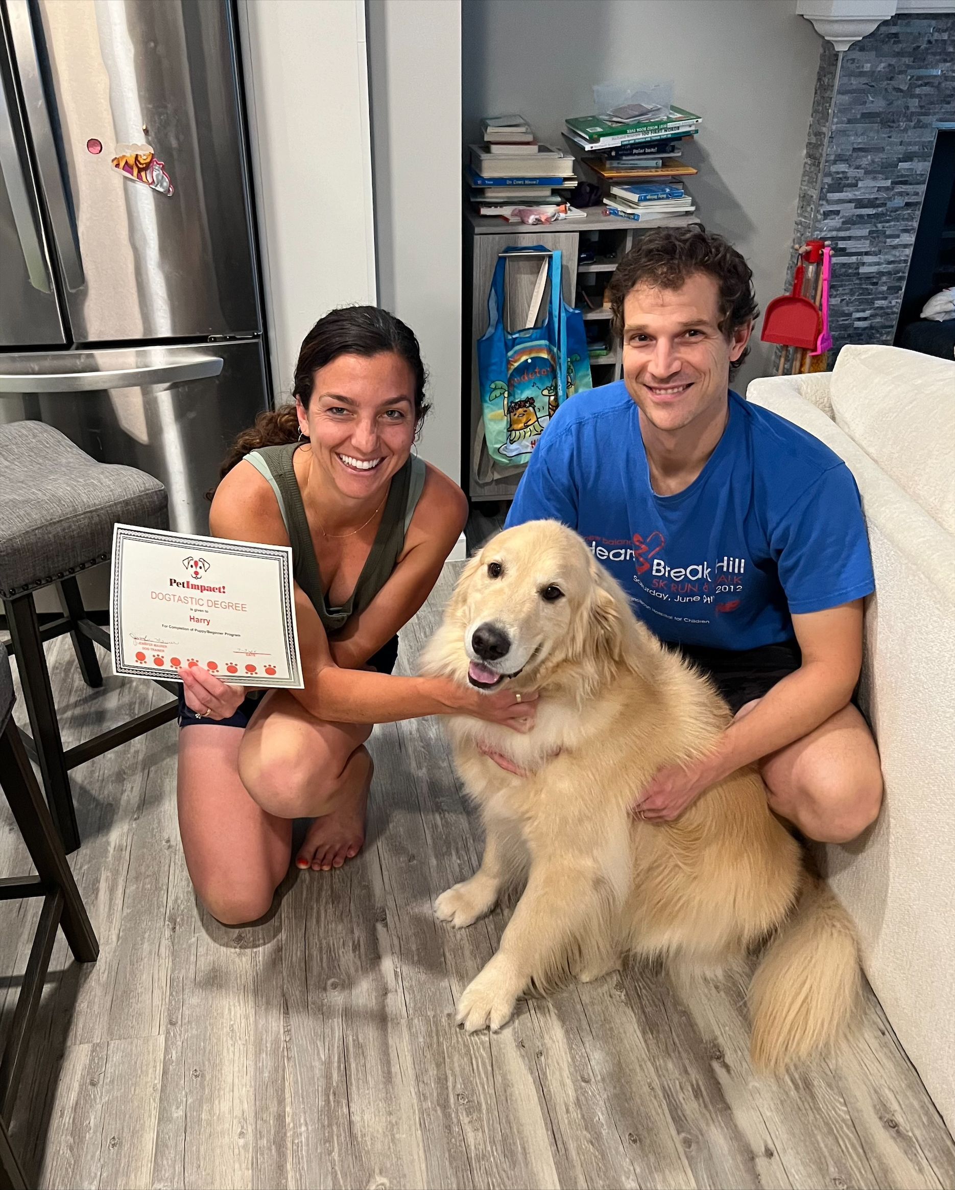 A man and a woman are kneeling down next to a dog holding a birthday cake.