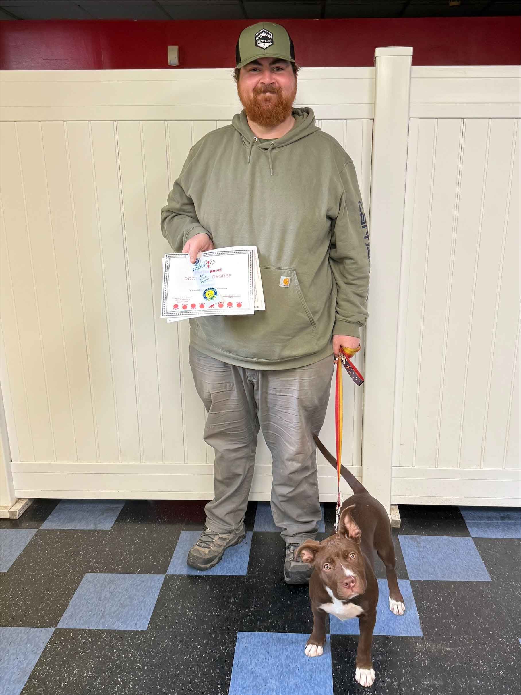 A man is standing next to a dog on a leash and holding a certificate.