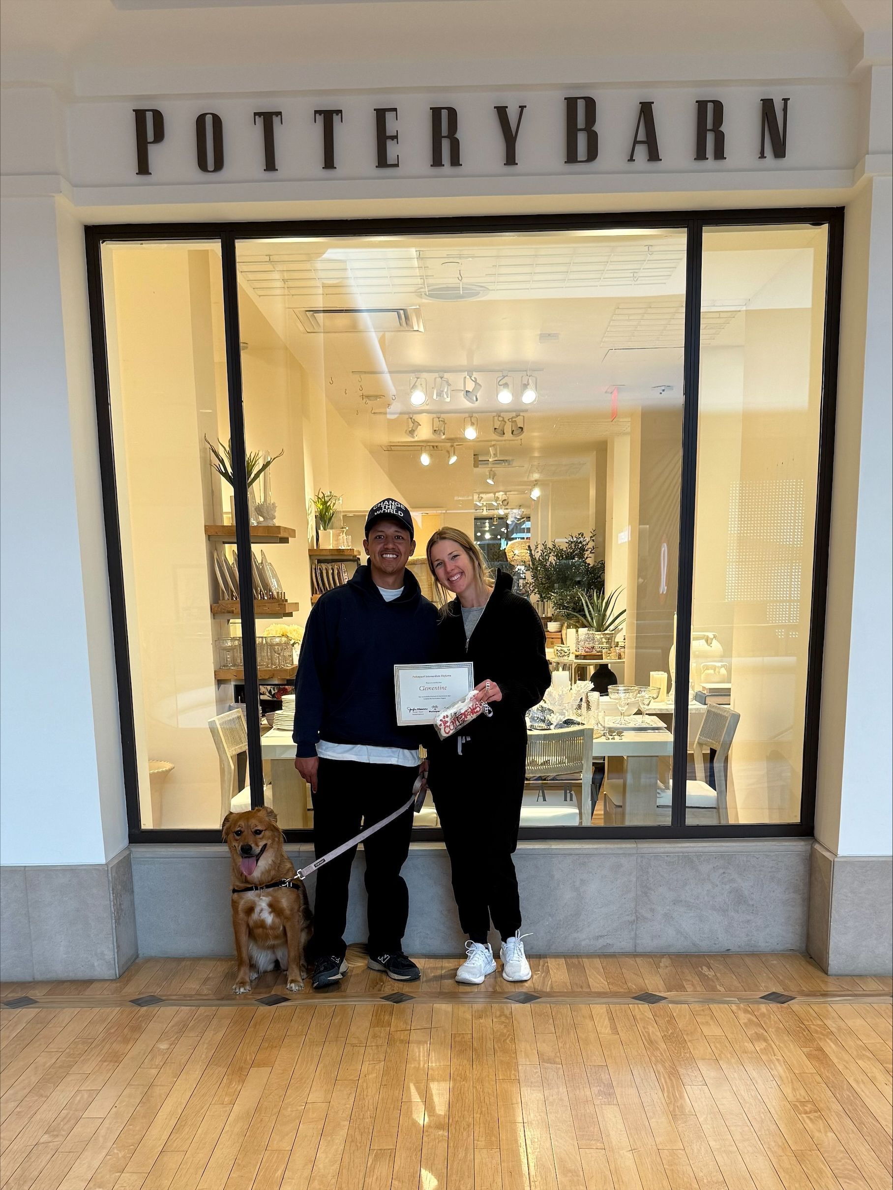A man and woman are standing in front of a store with a dog.