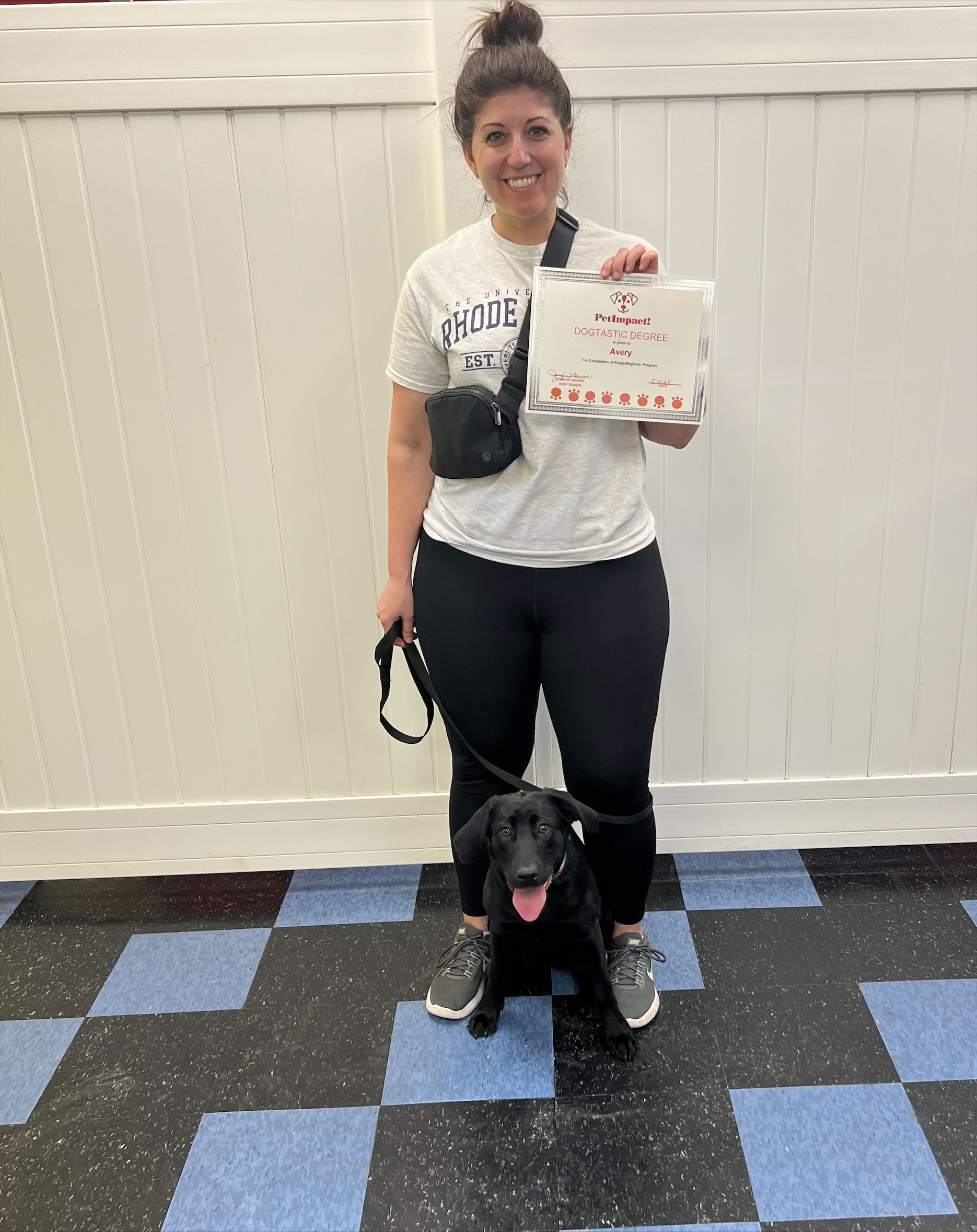A woman is standing next to a black dog and holding a certificate.
