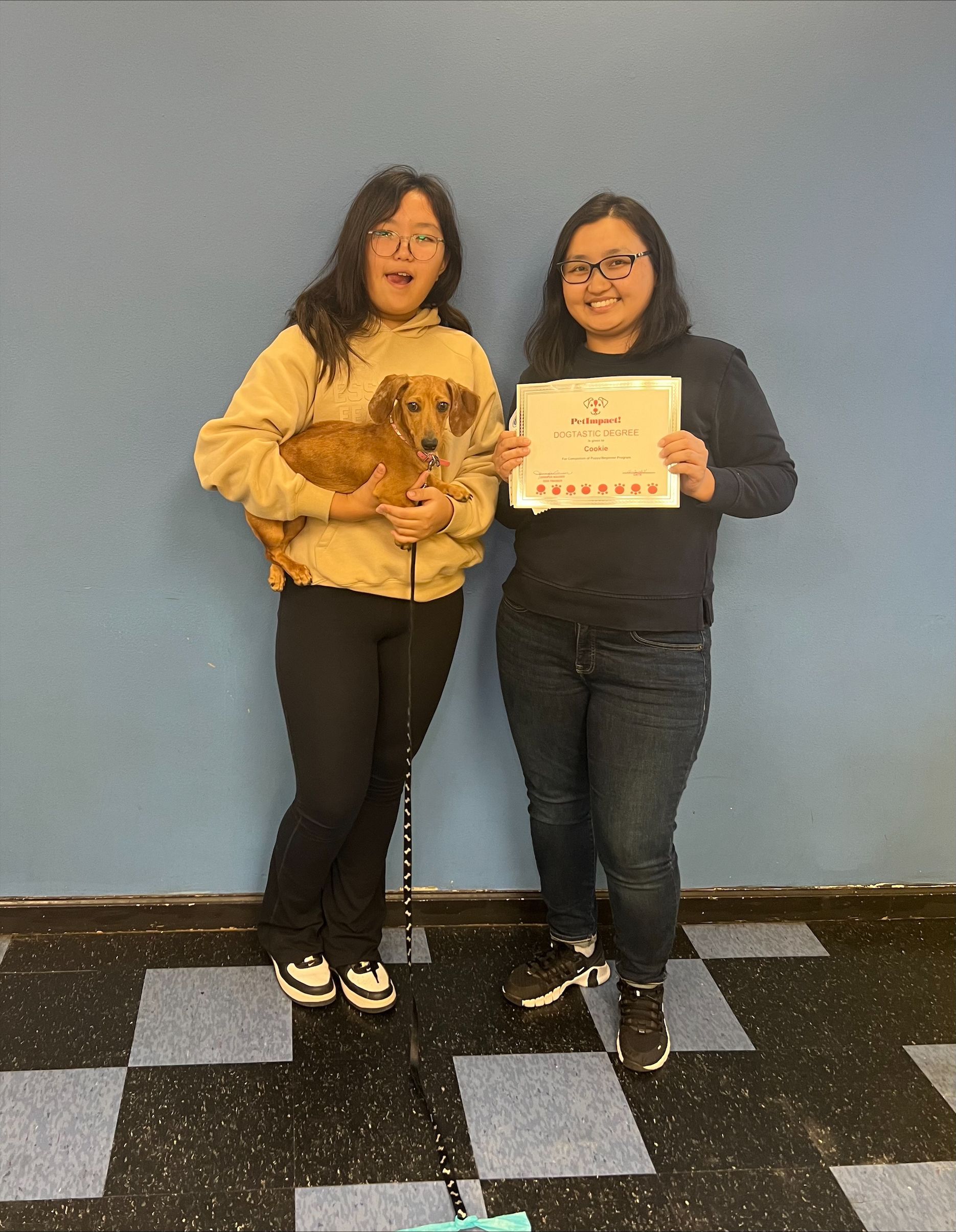 Two Women Are Standing Next to Each Other Holding a Dog and A Certificate.
