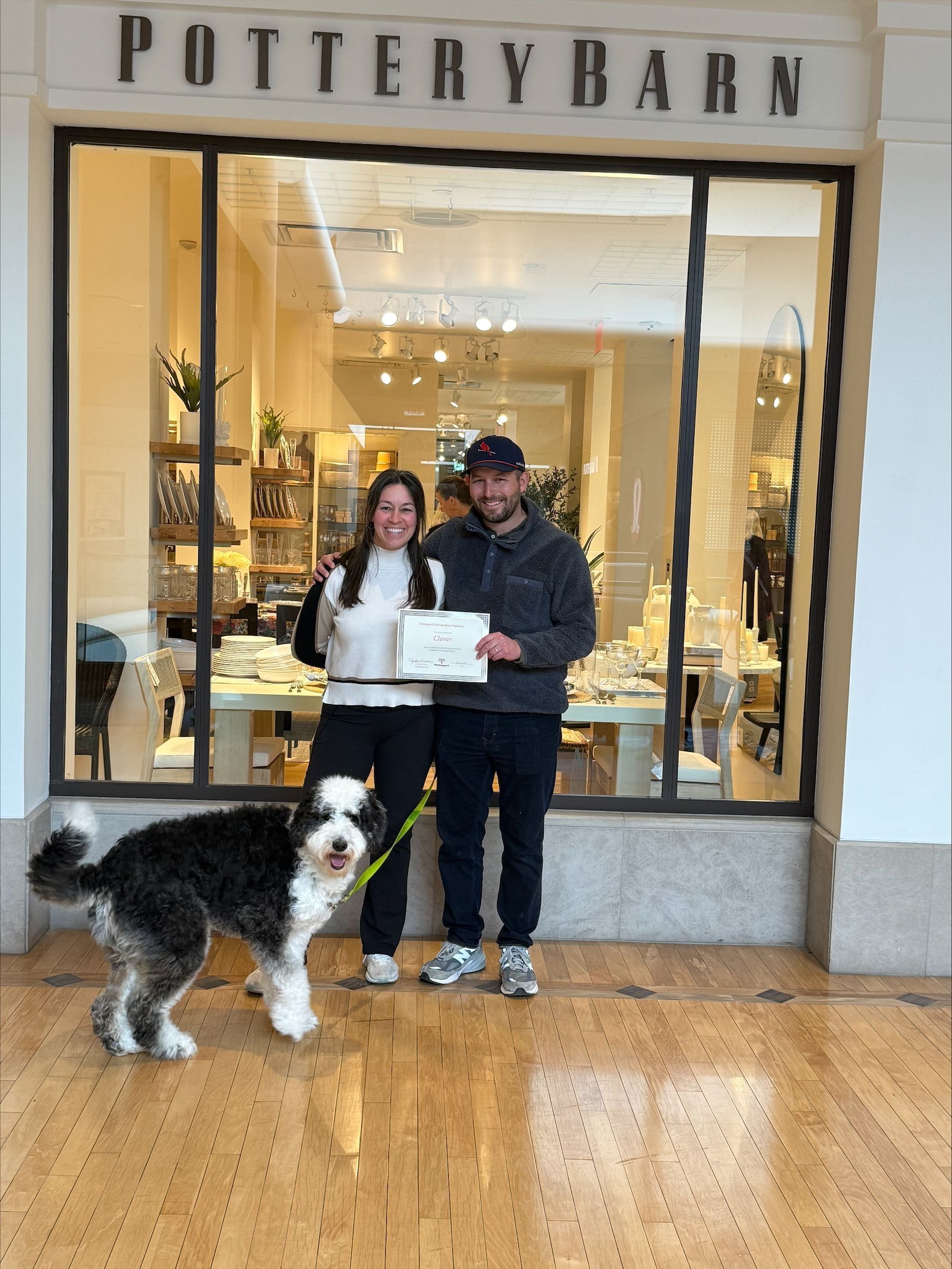 A man and woman are standing in front of a store with a dog.