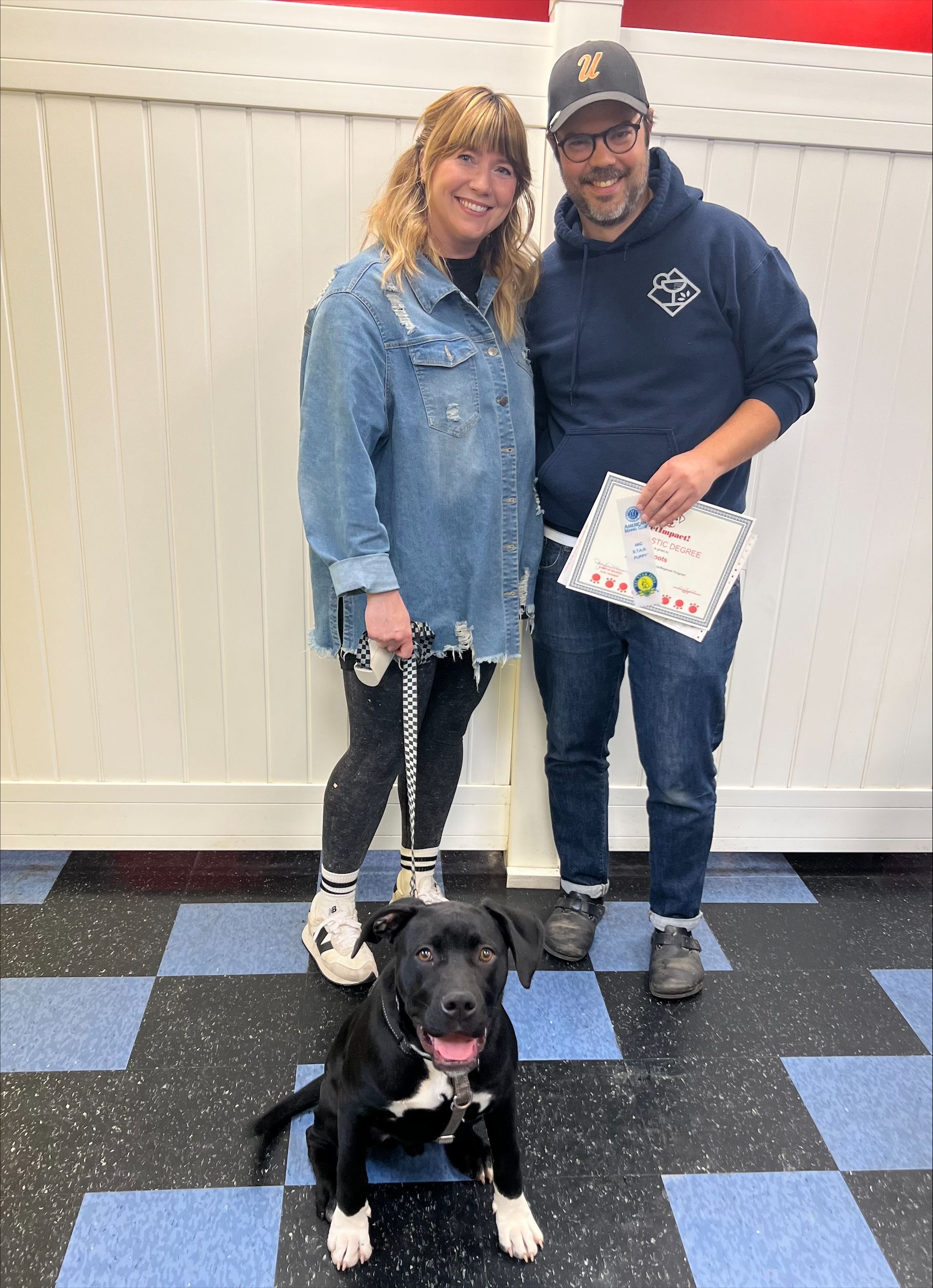 A man and a woman are standing next to a black and white dog.