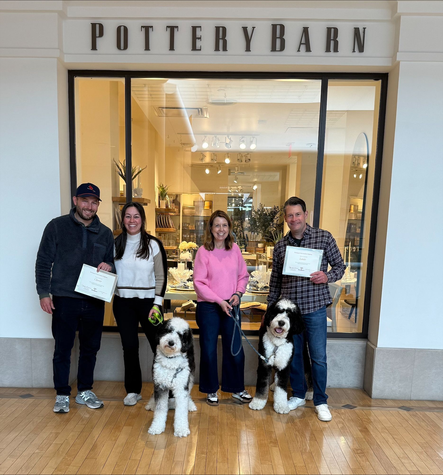 A man and woman standing next to a dog in front of a pottery barn store.