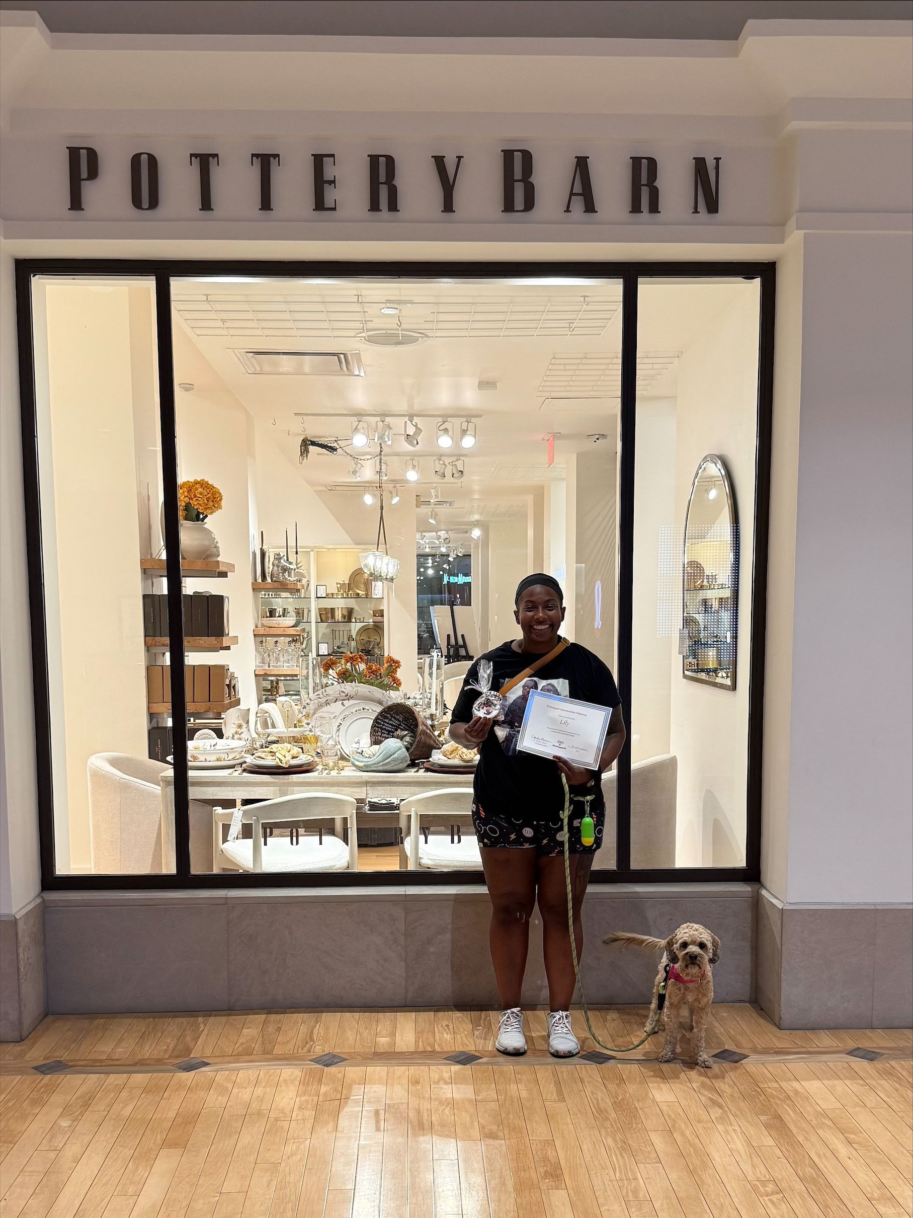 Woman and dog stand in front of a Pottery Barn store. The woman holds a certificate.