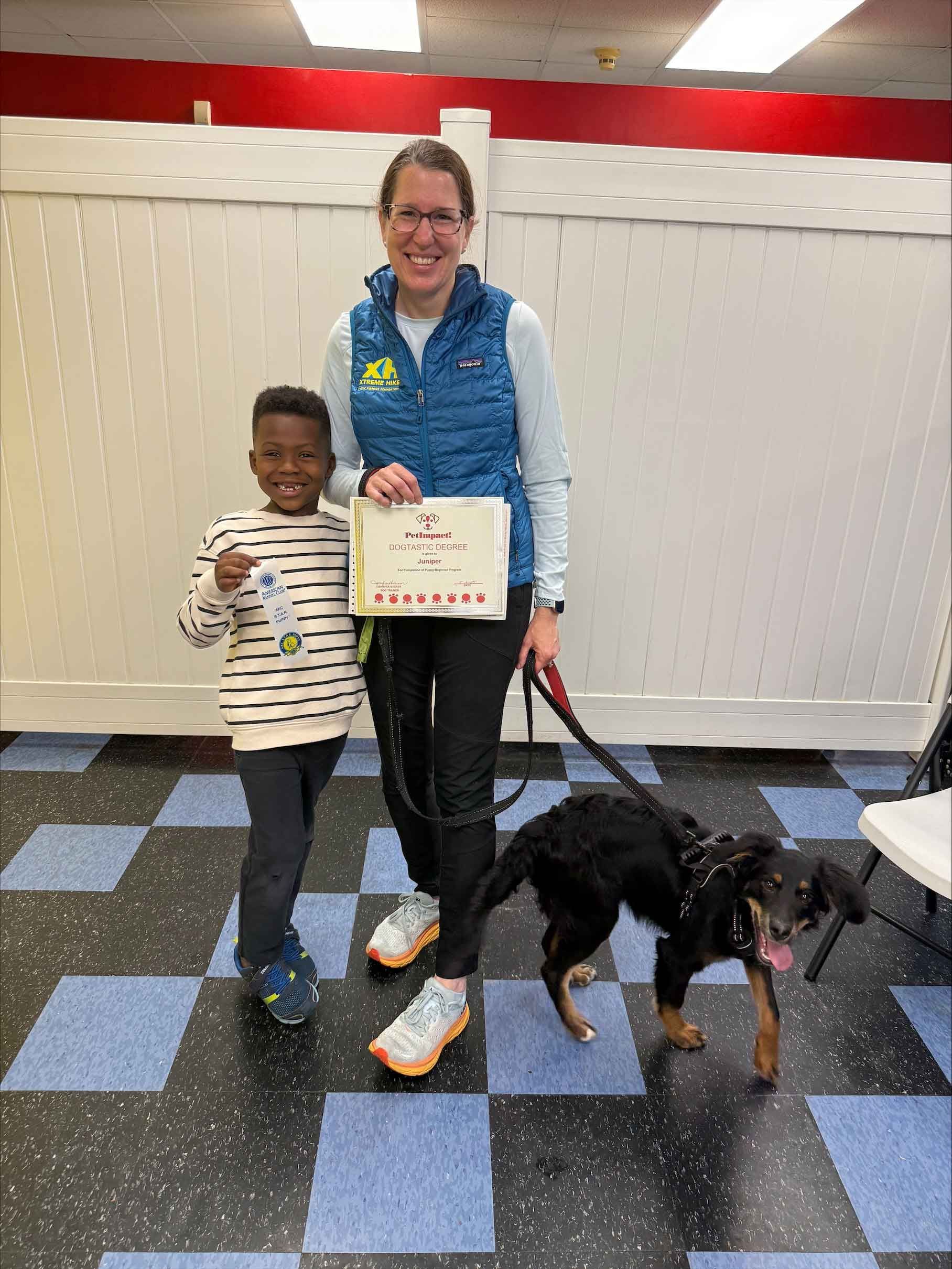 A woman and a child are standing next to a dog on a leash.