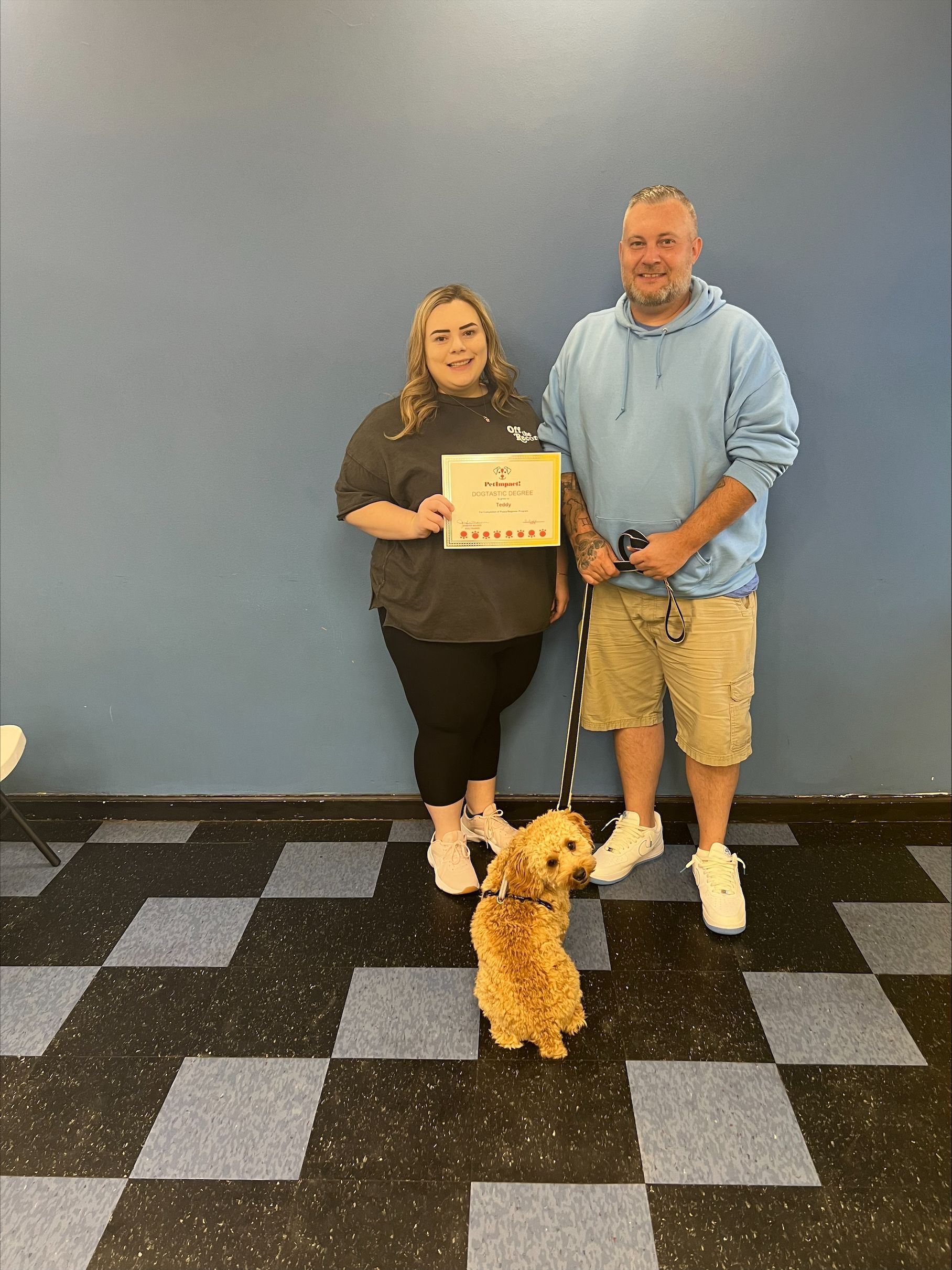 A man and a woman standing next to a small dog holding a certificate.