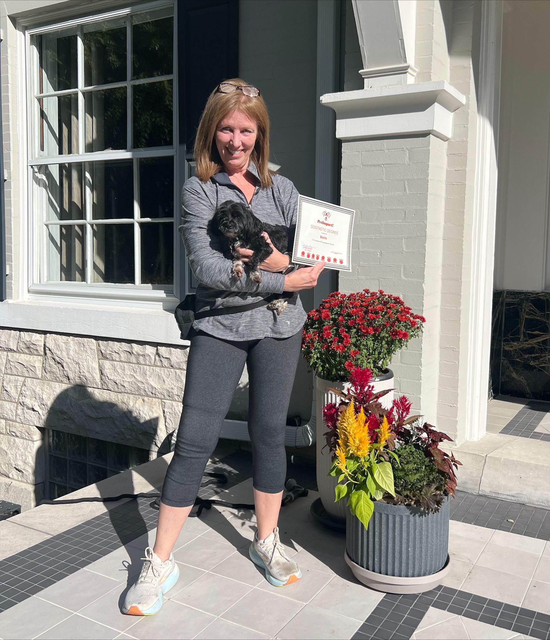 A woman is holding a dog and a box of toilet paper in front of a house.