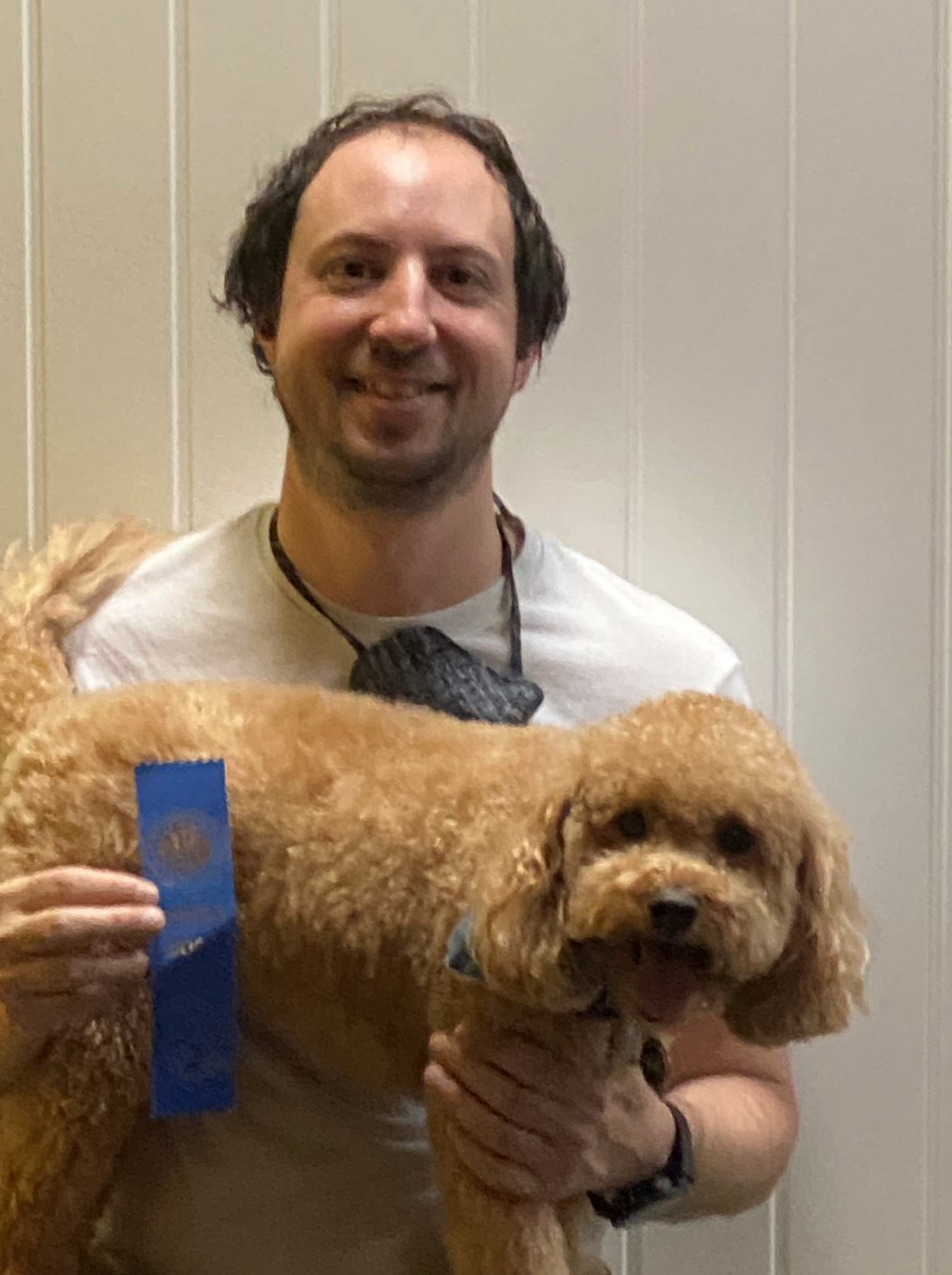 Man holding a fluffy brown dog, both smiling, with a blue ribbon.