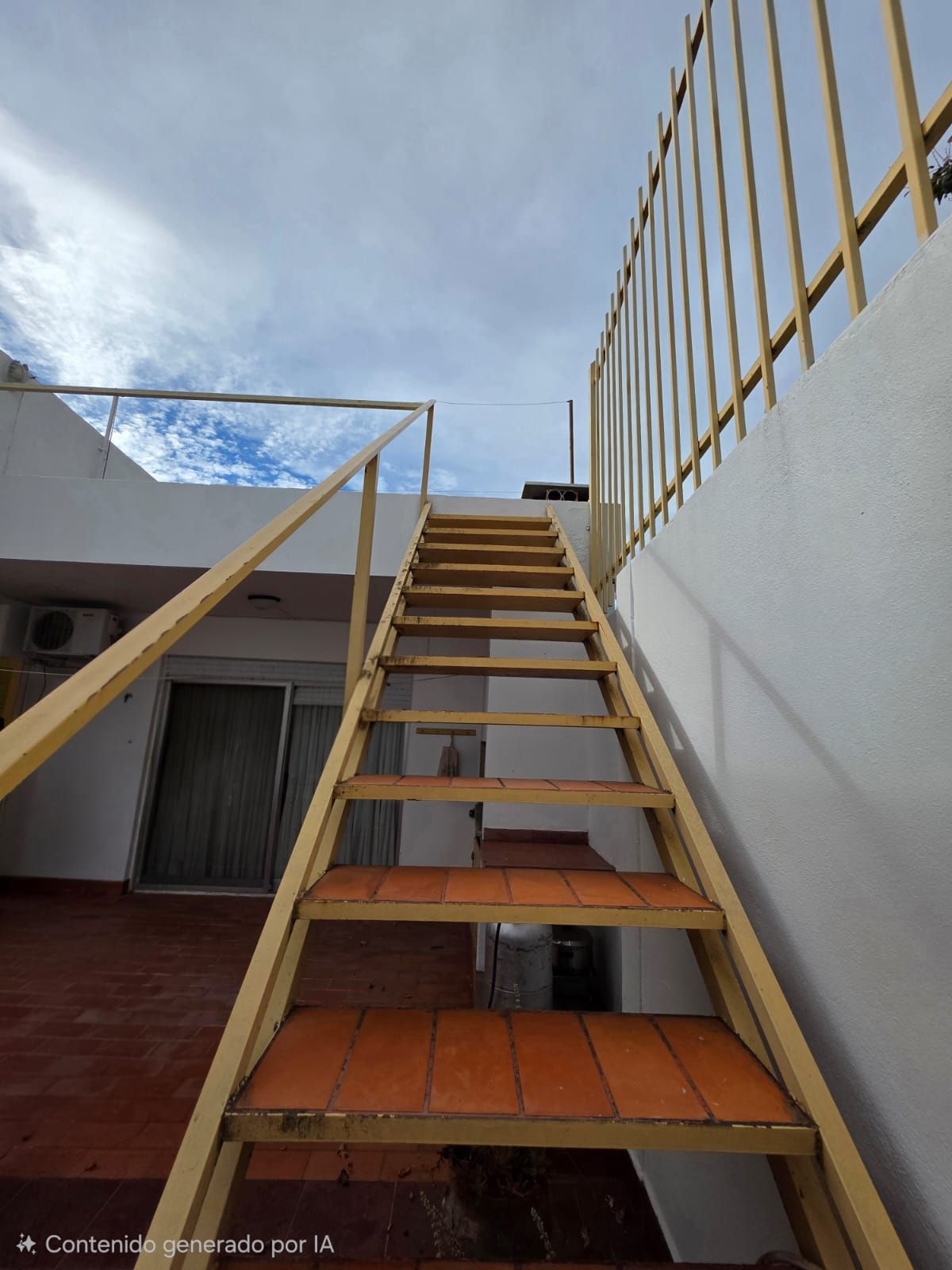 Escalera exterior empinada con escalones de madera y barandillas doradas junto a un edificio blanco bajo un cielo nublado.