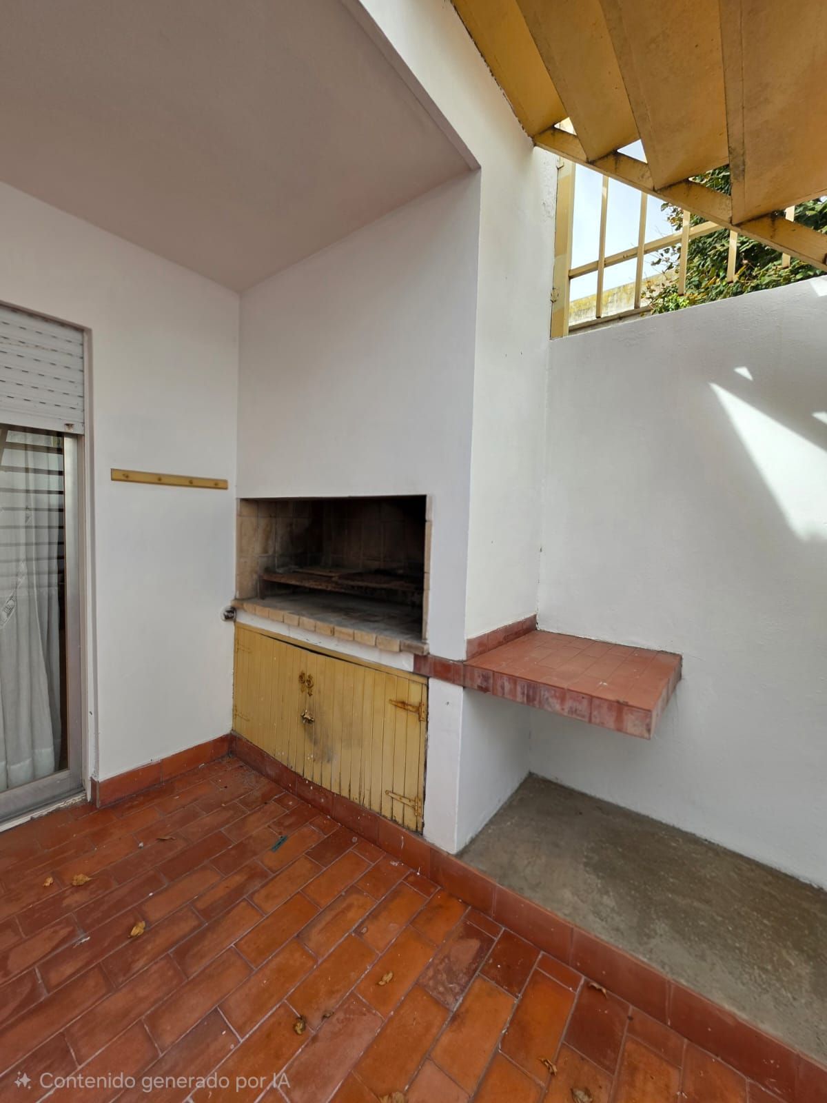 Patio cubierto con barbacoa de ladrillo, paredes blancas, techo de madera y suelo de terracota.