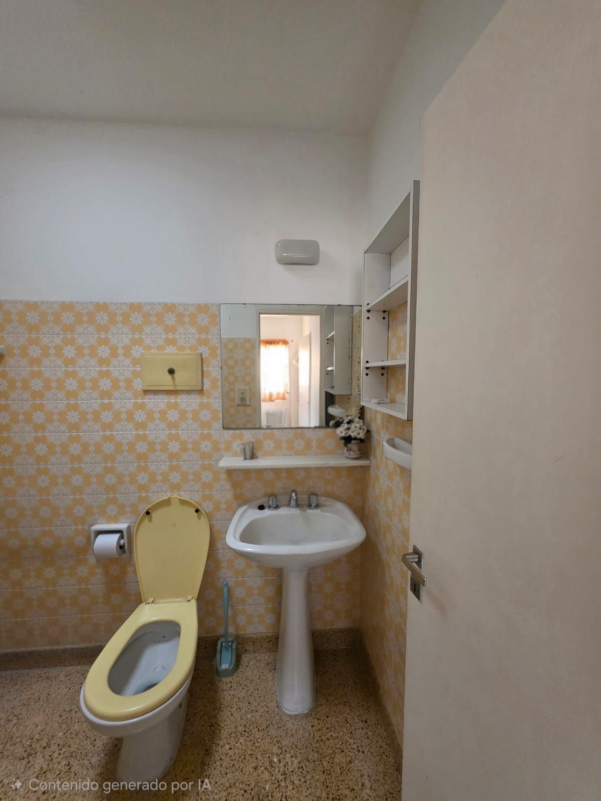 Baño pequeño con inodoro, lavabo con pedestal, espejo y azulejos amarillos estampados hasta la mitad de la pared.
