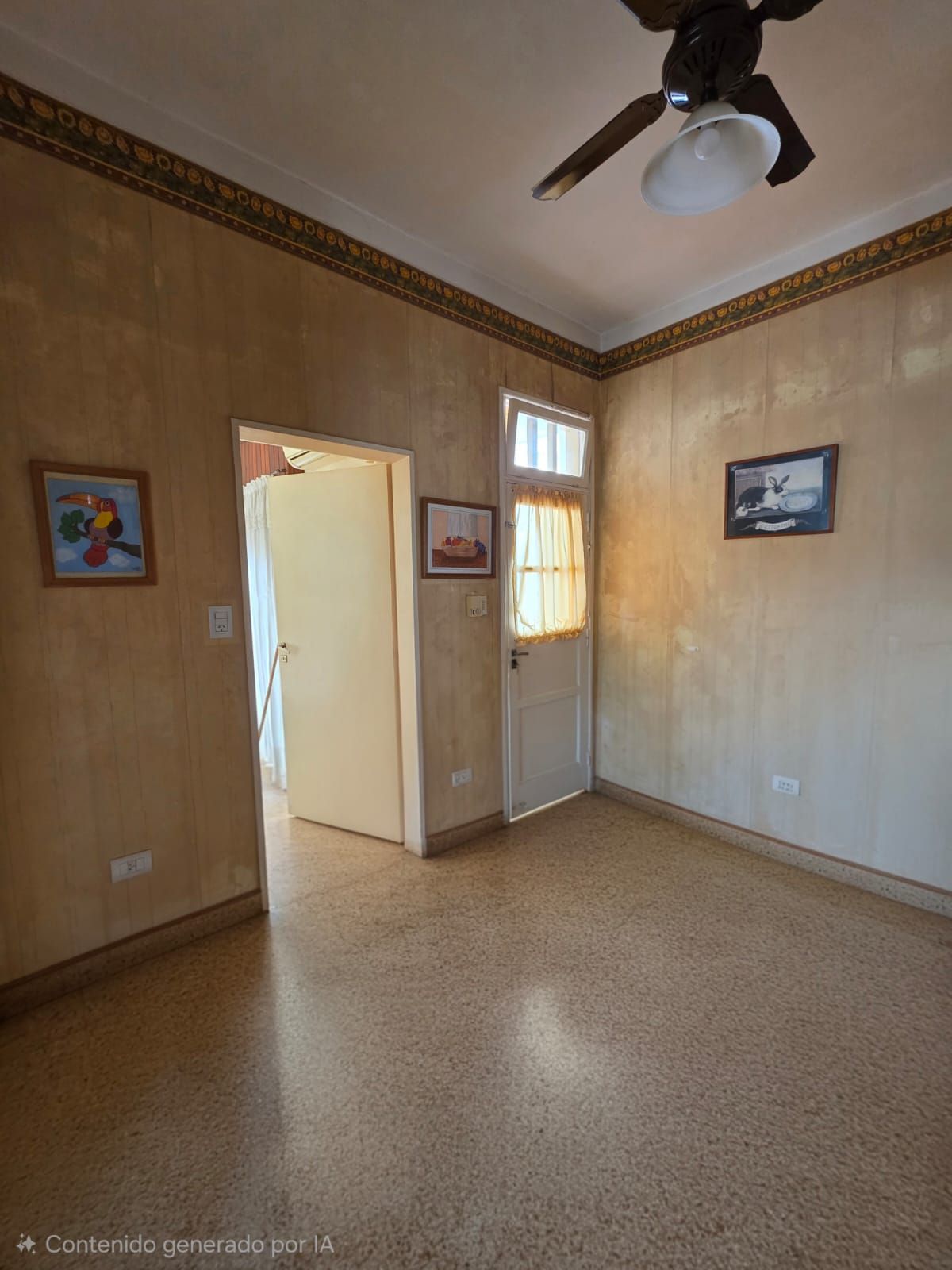 Habitación vacía de color beige con suelo de baldosas, ventilador de techo y cuadros enmarcados en las paredes.
