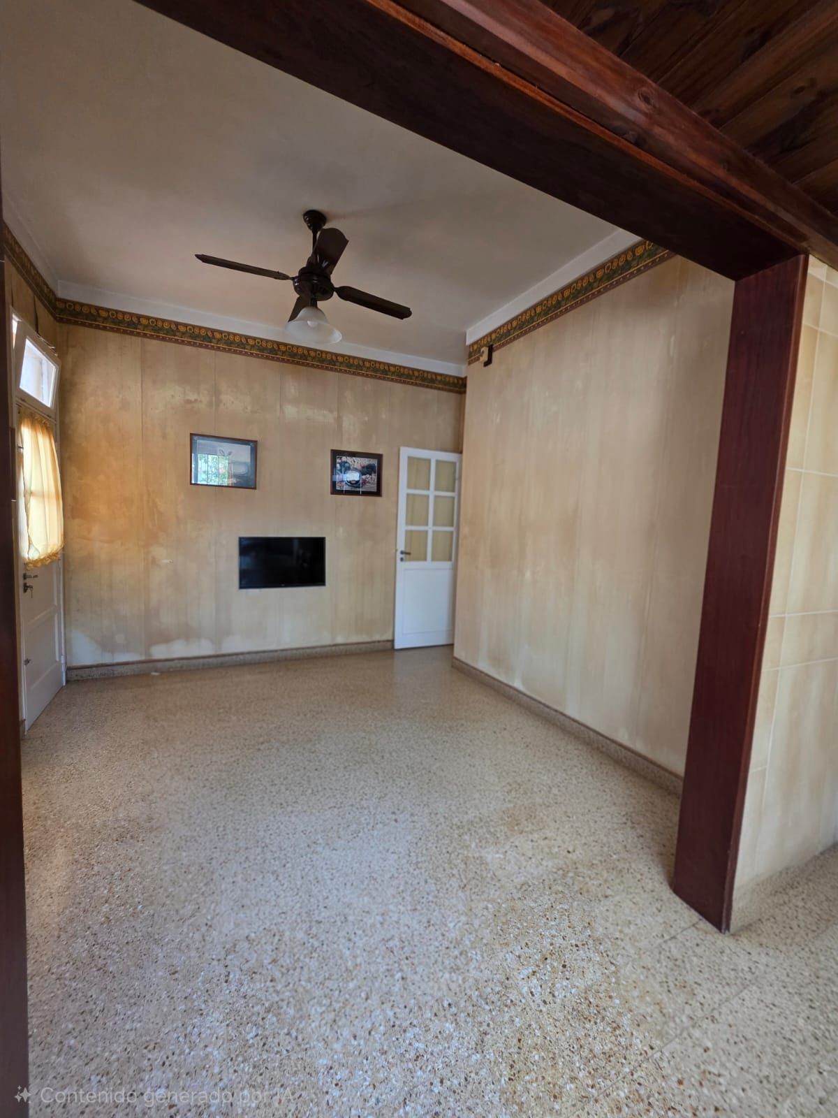 Sala de estar vacía con paredes beige, suelo de terrazo, ventilador de techo, chimenea y puerta blanca.